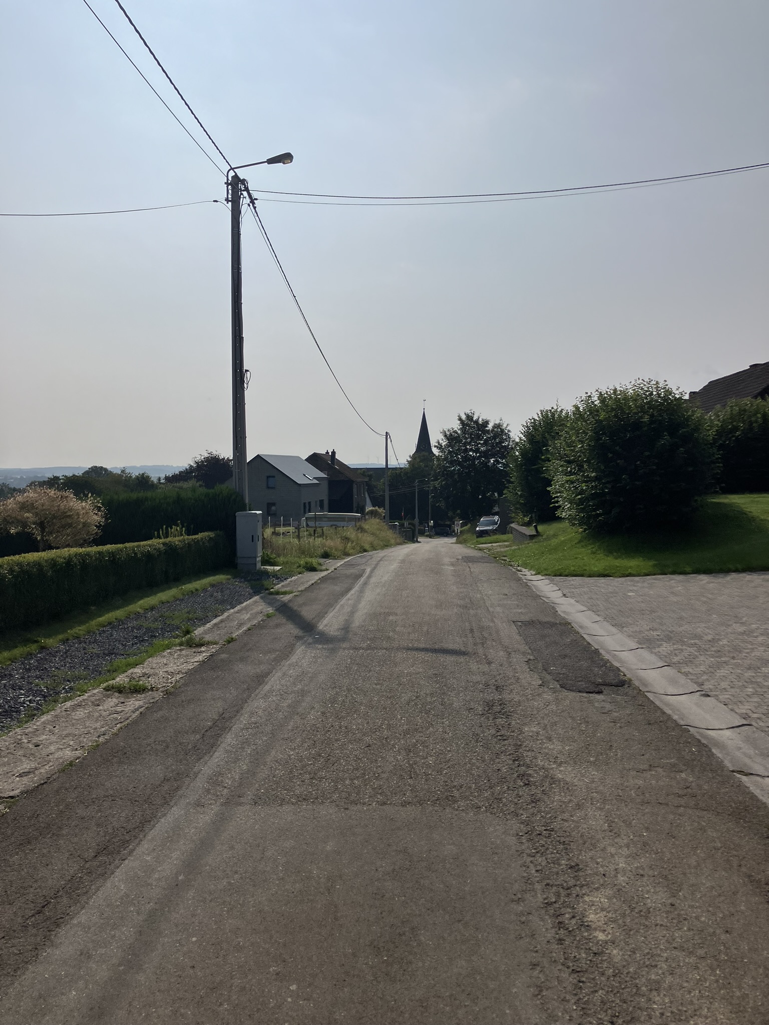Bikepacking Belgien - Kleine Dorfstraße in Montleban in Belgien mit Steinhäusern, Kirchturm im Hintergrund und ruhiger Atmosphäre.