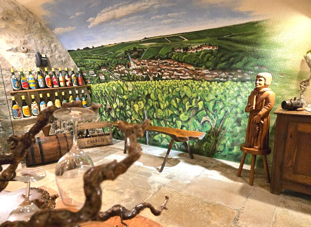 Trompe-l'œil mural d'un paysage de vignes intégré dans la décoration d'un musée du vin avec bouteilles et statues.