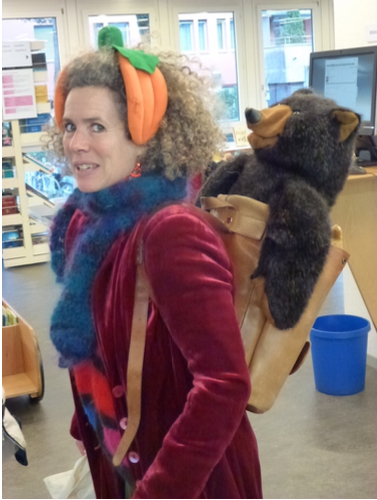 Teaching Artist auf dem Weg zur Schulklasse – mit Plüschbär im Rucksack, farbenfrohem Outfit und einem Lächeln voller Vorfreude.