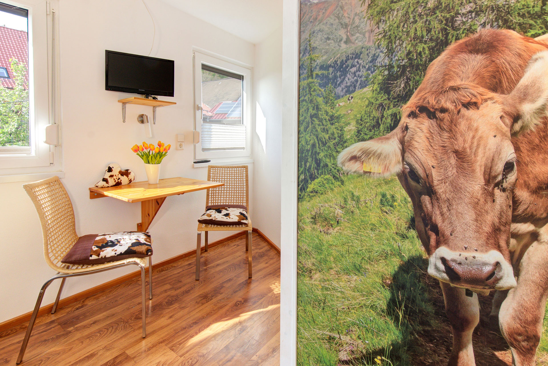 kuhposter seitlich mit blick auf private zweier Sitzgruppe mit Tulpenstrauss vor Tv in Ferienwohnung