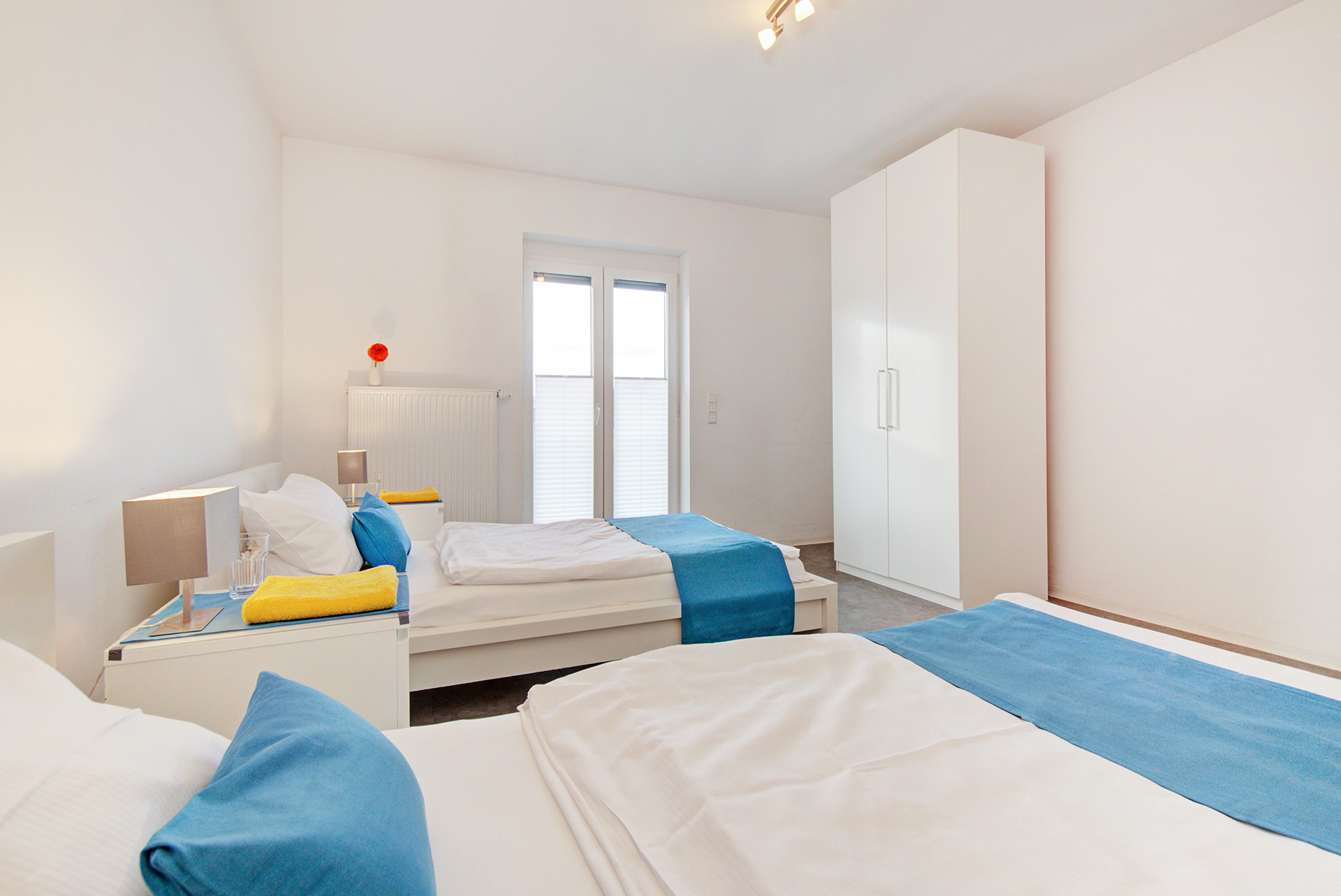 monteurzimmer fotografieren zwei einzelbetten mit blick aufs fenster türkisfarbene bettläufer und kissen