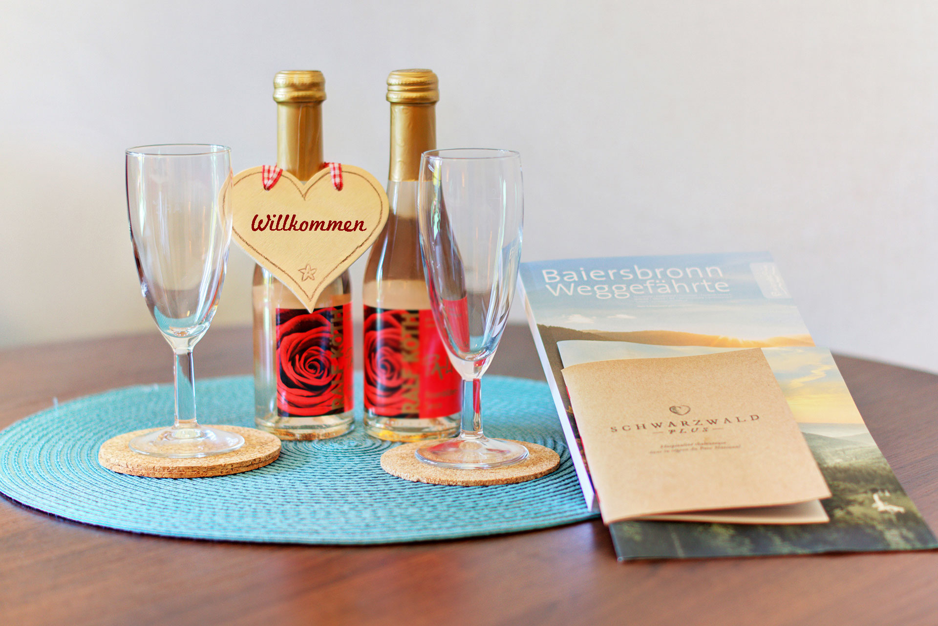Willkommensschild an kleiner Sektflasche mit Arrangement aus Gläsern