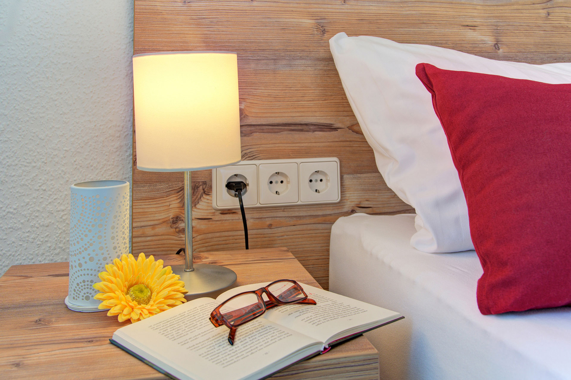 Nachttisch Doppelzimmer mit Lampe Buch Brille und gelber Gerbara