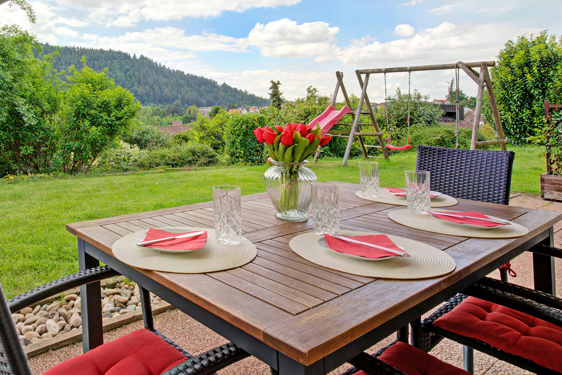 terrasse mit sitzgarnitur und rotgedecktem tisch sowie roter tulpenstrauss in ferienwohnung