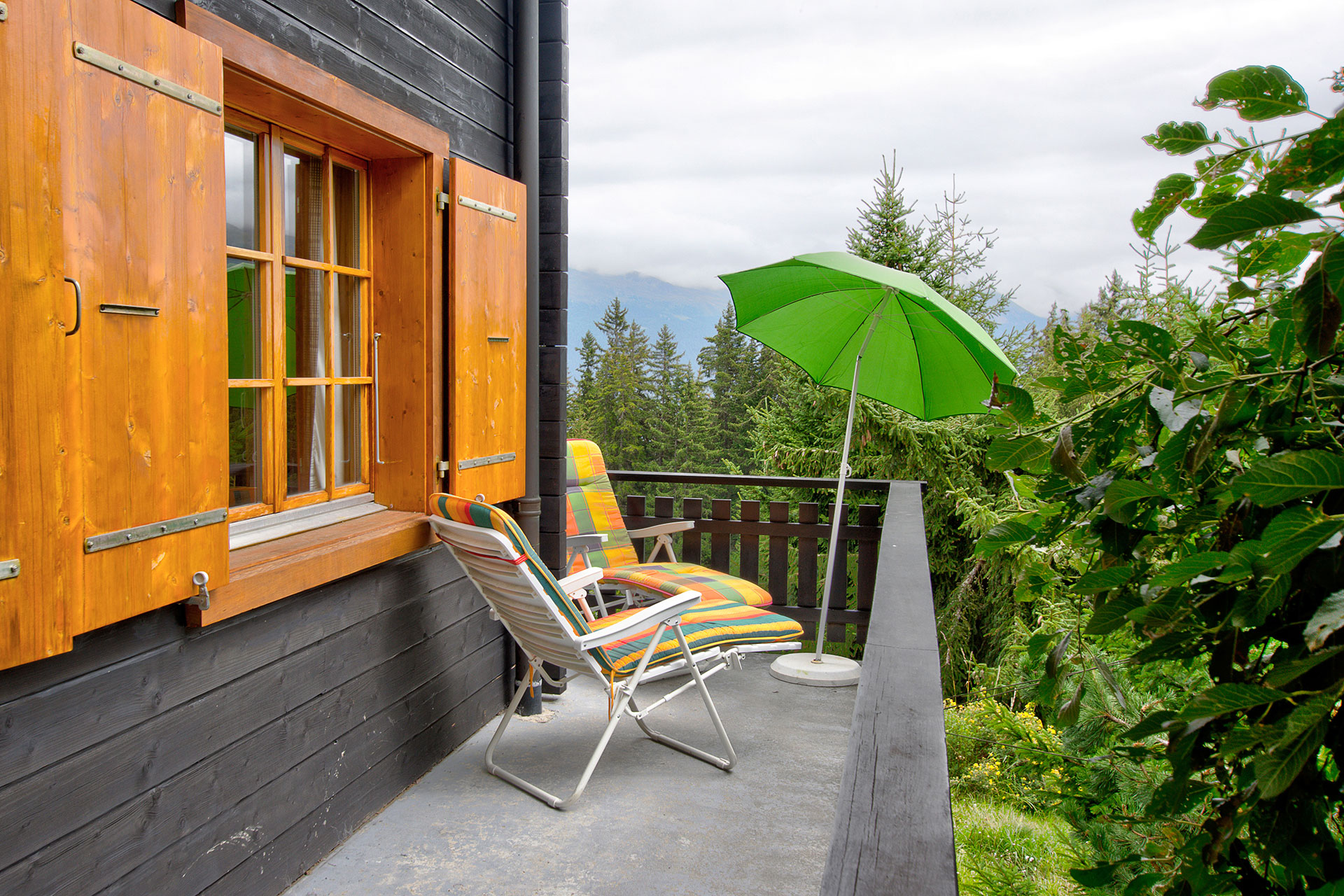 ferienhaus foto holzchalet mit balkon und gruenem schirm vor bergparnorama