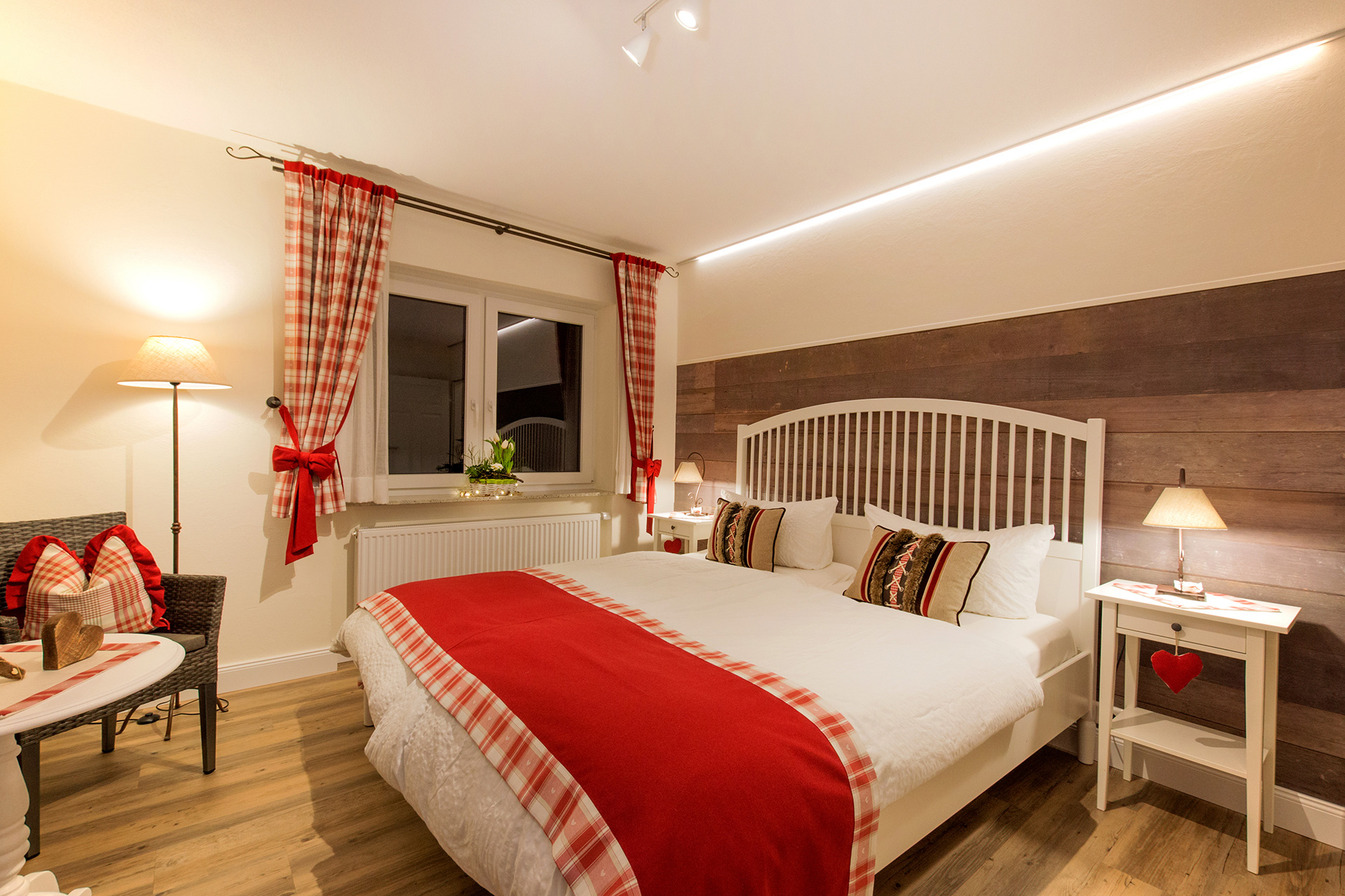 doppelbett mit rotem bettfläufer am abend und dunkles fenster in ferienwohnung 
