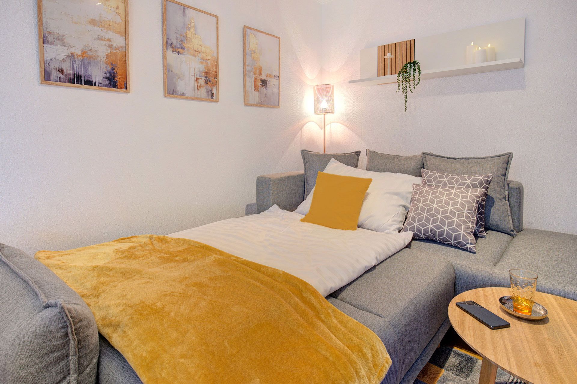 bezogenes graues sofabett mit okkerfarbener ueberdecke und kissen