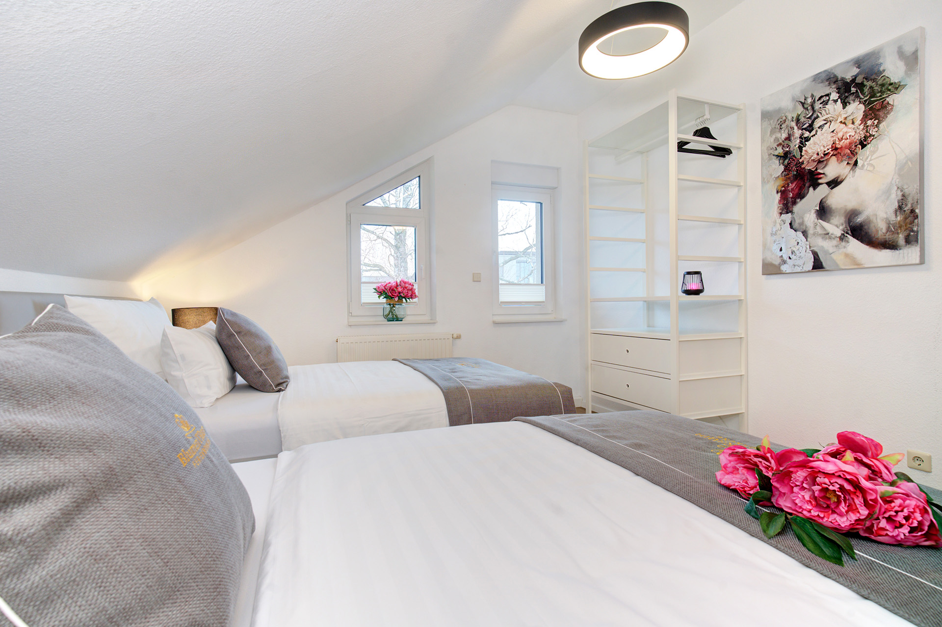 Schlafzimmer mit drei Betten graue Bettäufer sowie Blick zum Regal und Fenster der ferienwohnung