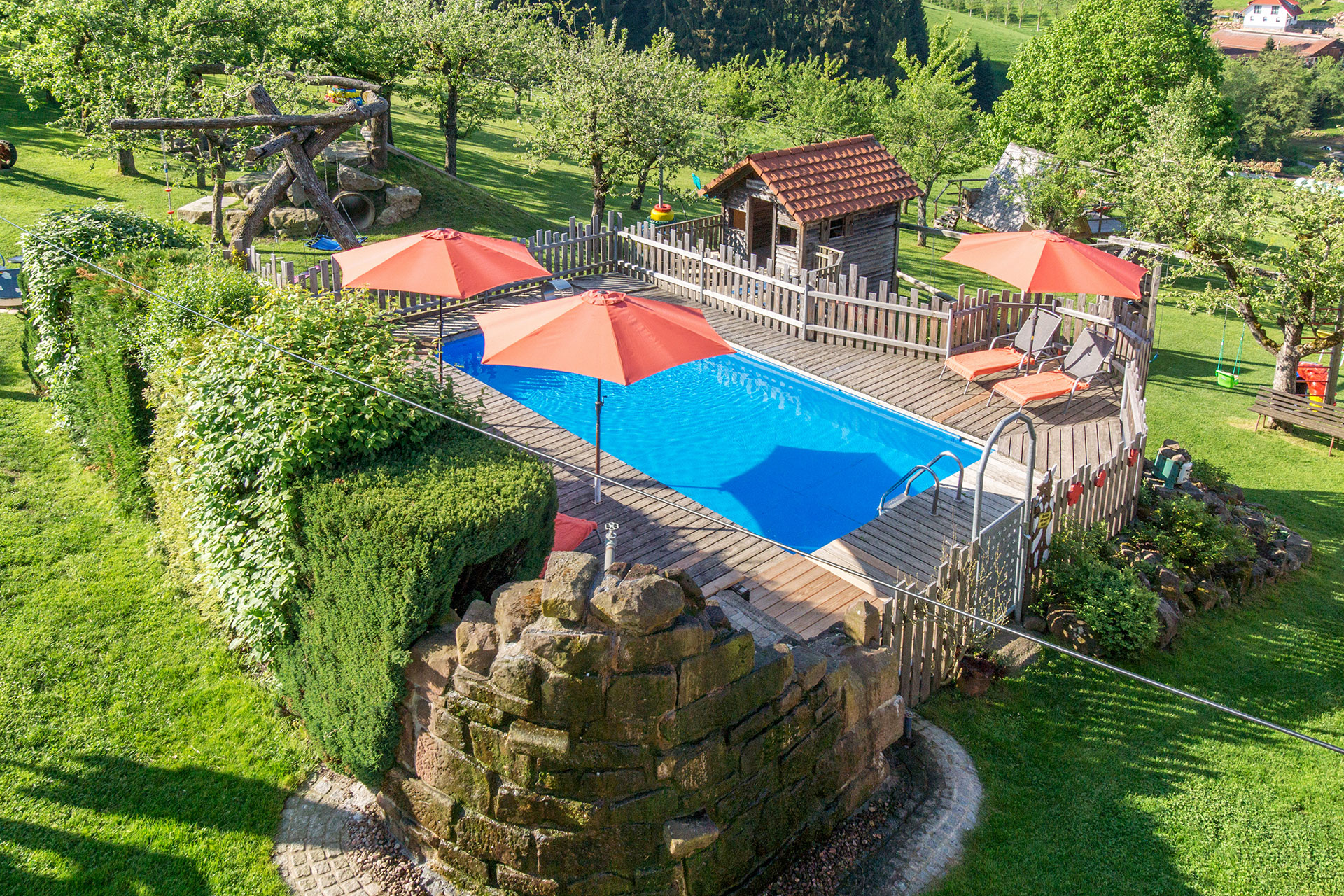 naturpool am ferienhaus mit roten Sonnenschirmen