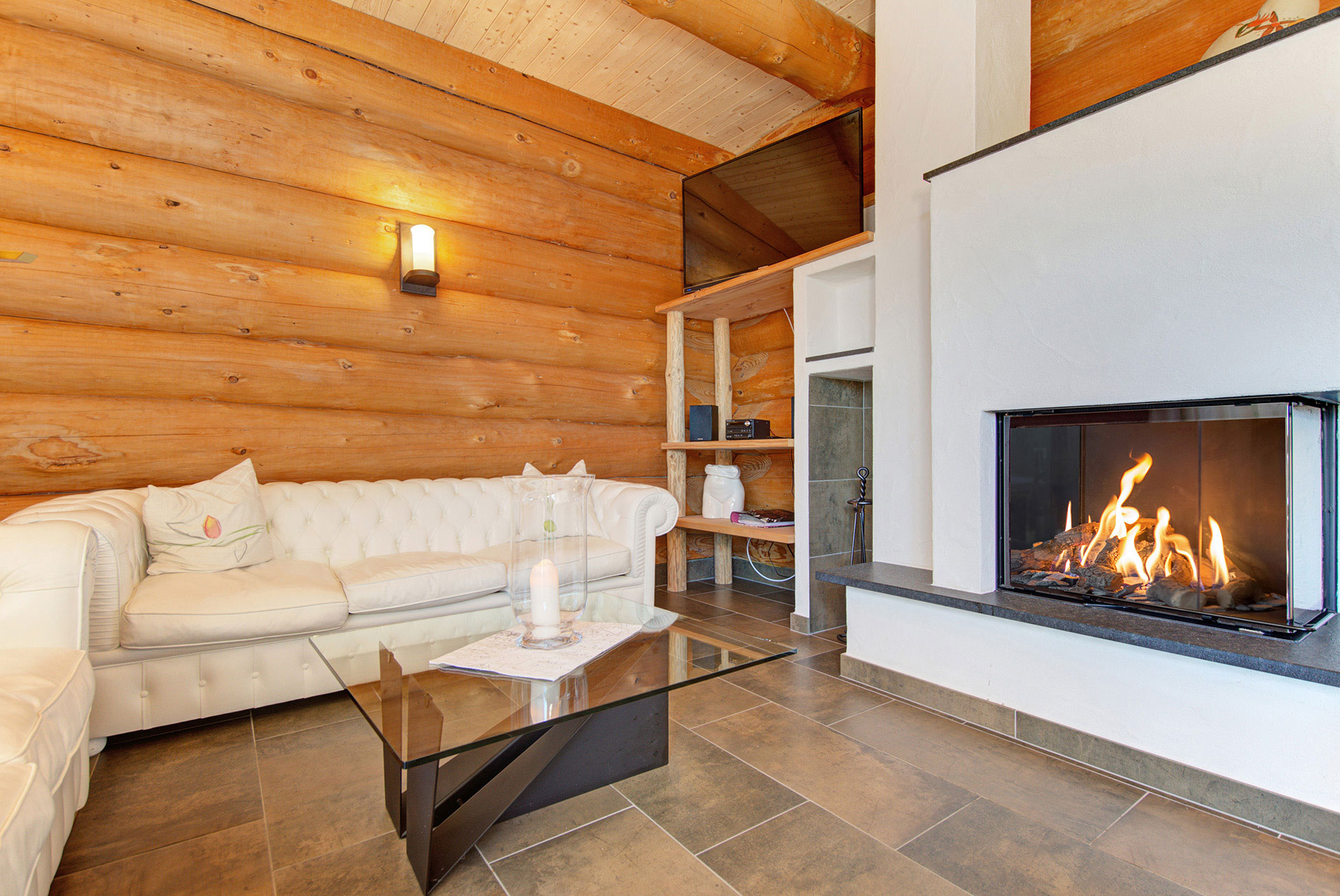 Gemütliches Ferienhaus-Wohnzimmer mit Holz, cremefarbenem Ledersofa und Kaminfeuer mit Bildbearbeitung
