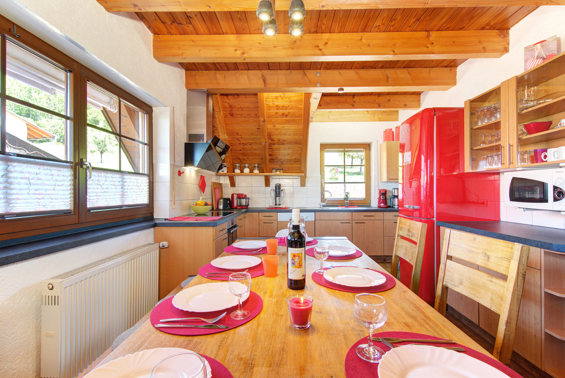 rot eingedeckter holztisch mit stühlen und blick zur Küche im ferienhaus