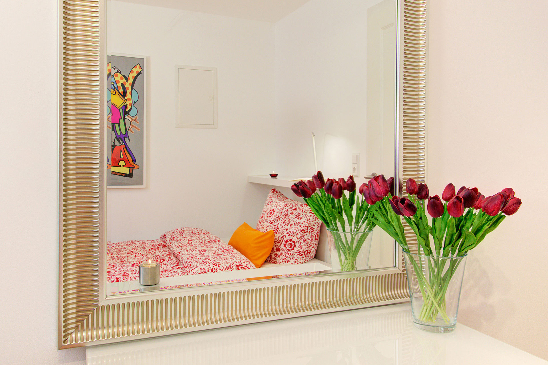 apartment fotografin blick in den spiegel mit roten tulpenvase auf einzelbett mit bild