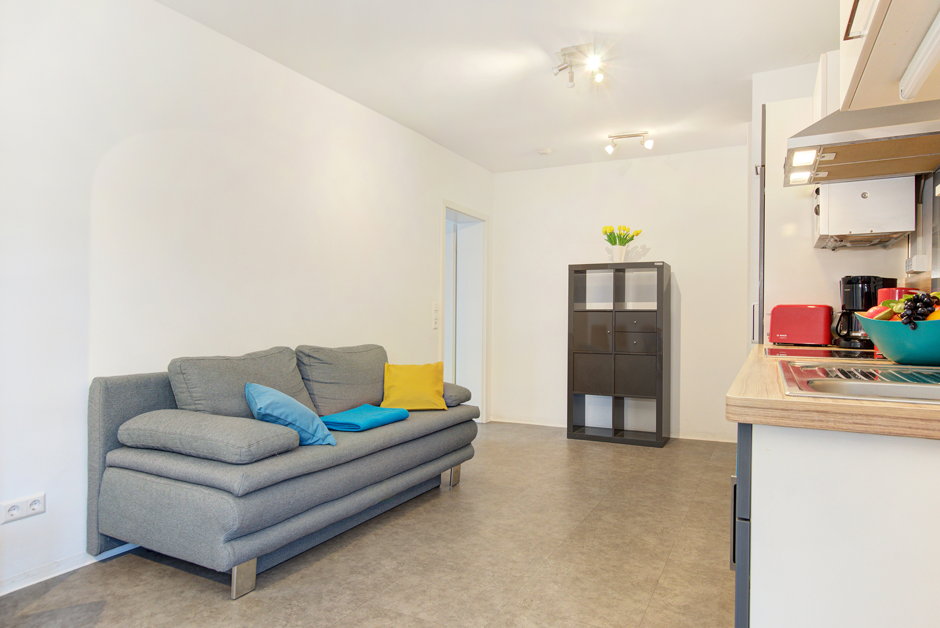 monteurzimmer fotografieren graues sofa mit dunklem regal und küchenzeile