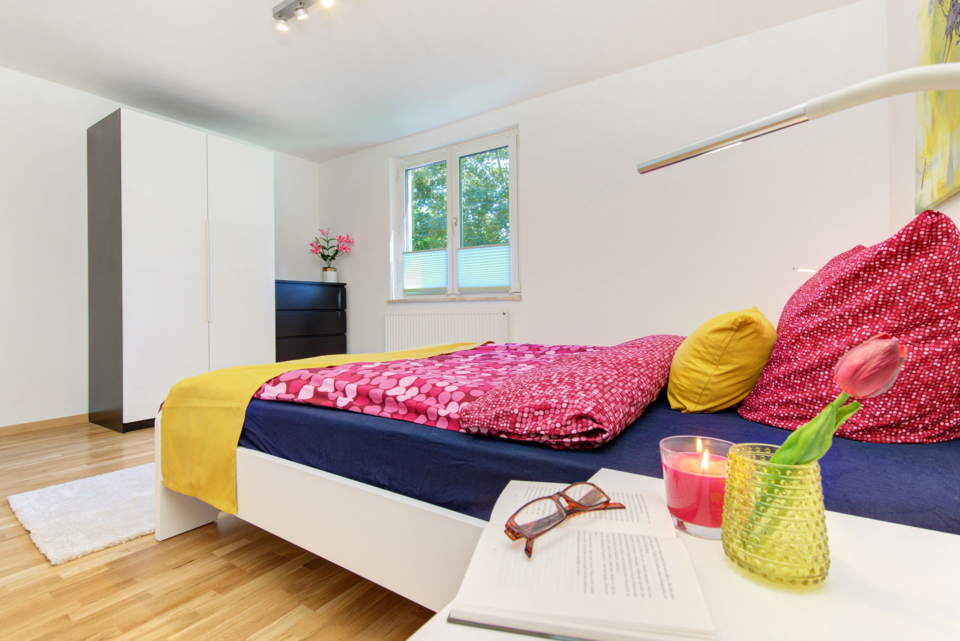 apartment fotografieren schlazfzimmer nachttisch mit tulpe in vase teelicht buch und blick auf fenster