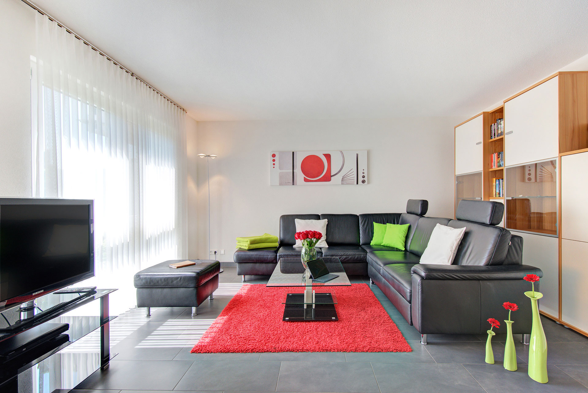 foto ferienwohnung wohnraum frontal mit schwarzem sofa roter teppich roter rosenstrauss