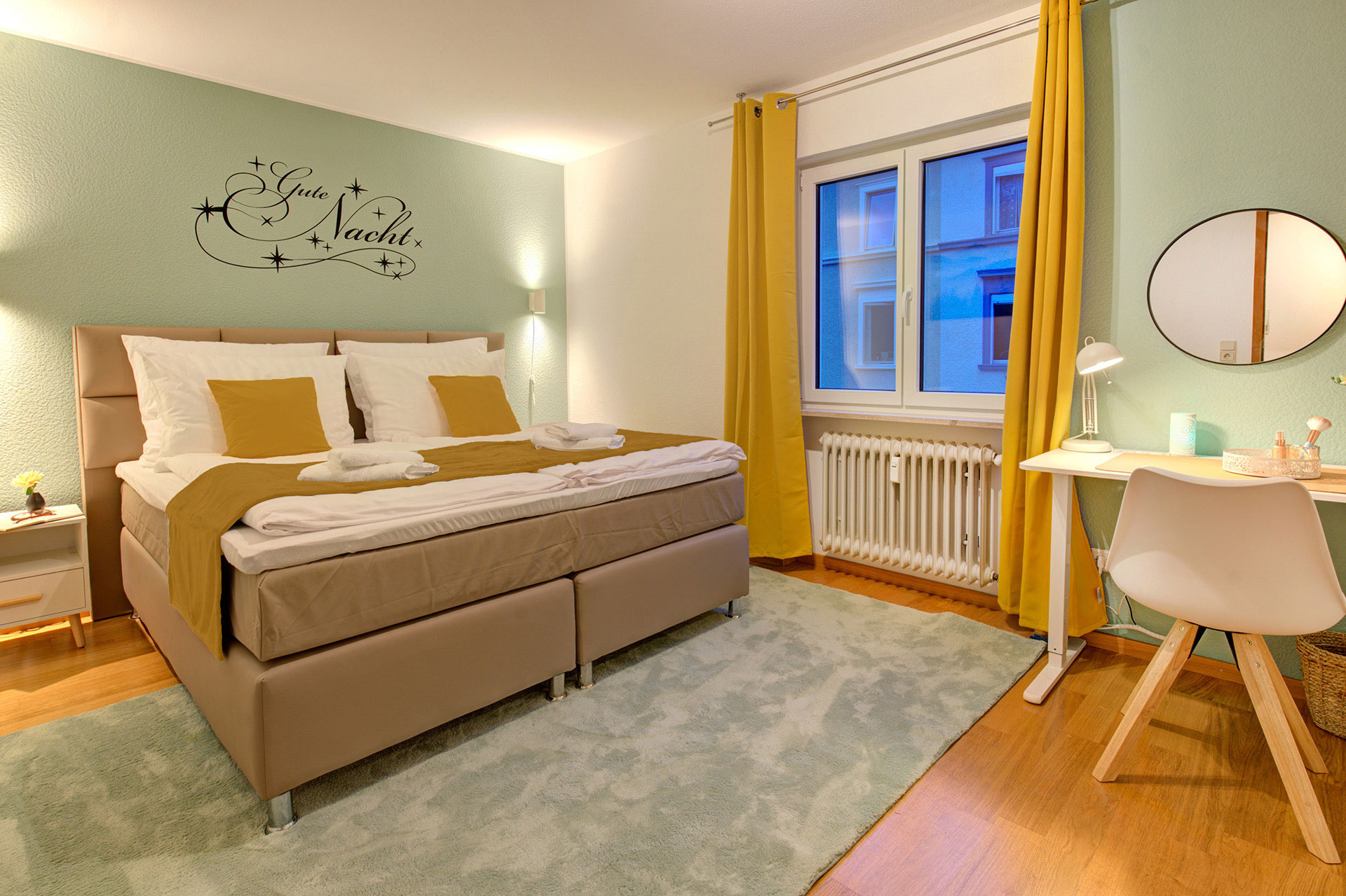 boxspringbett in Ferienwohnung mit okker farbenem kissen und bettläufer bei blauem Licht vom airbnb fotograf