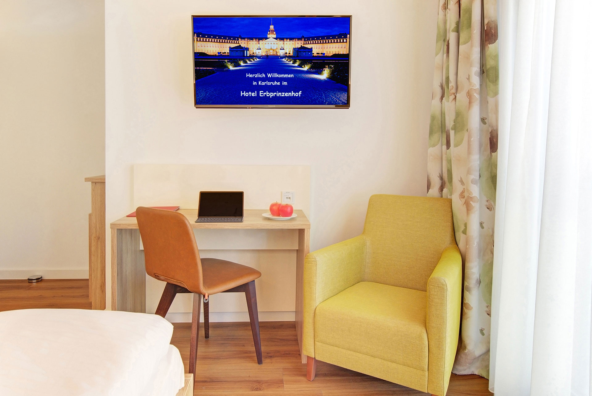 Arbeitsbereich im Hotelzimmer mit Schreibtisch, daneben ein TV-Monitor; auf dem Bildschirm das Wahrzeichen der Stadt als Grafik eingebettet
