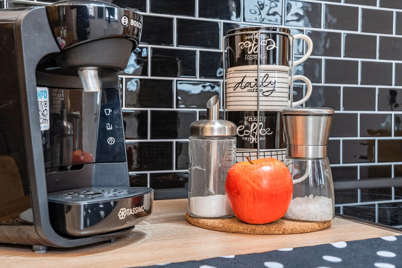 esspressomaschine und Tassenstapler davor ein roter Apfel und ein schwarzes Geschirrtuch mit weisen Punkten - ferienwohnung fotografieren