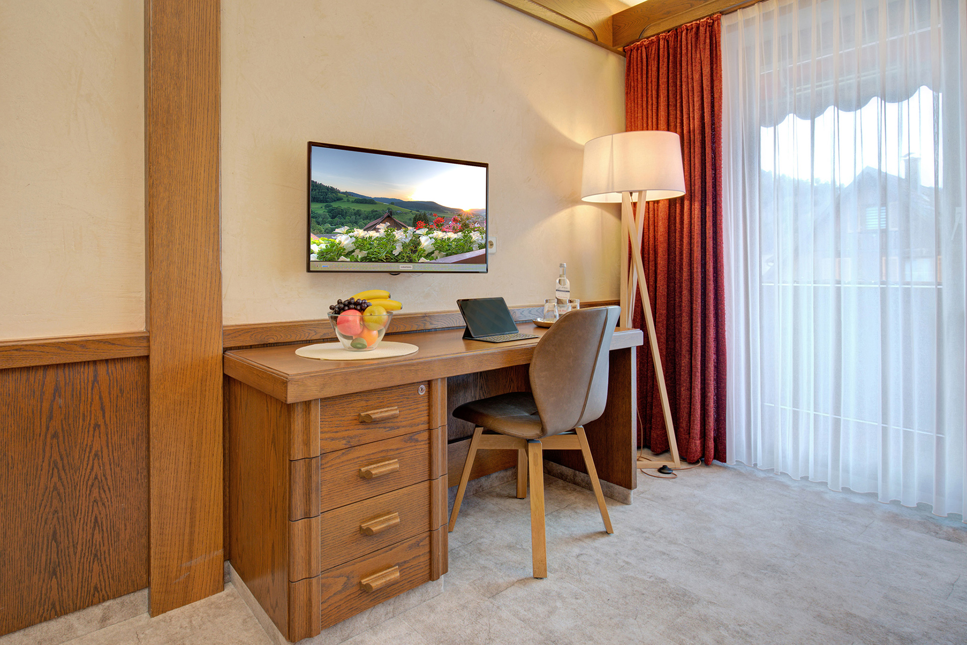 Arbeitsbereich aus Eiche rustikal im Hotelzimmer, Stehlampe daneben; Fernseher zeigt ein Landschaftsbild von Ferienhaus-Foto bearbeitet
