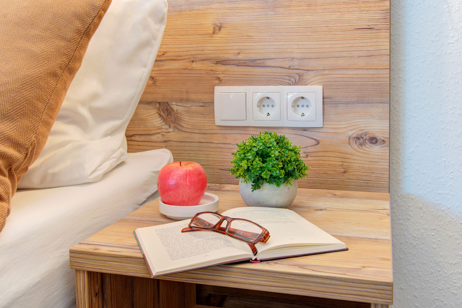 nachttisch doppelbett mit brille buch apfel und grünpflanze in studio