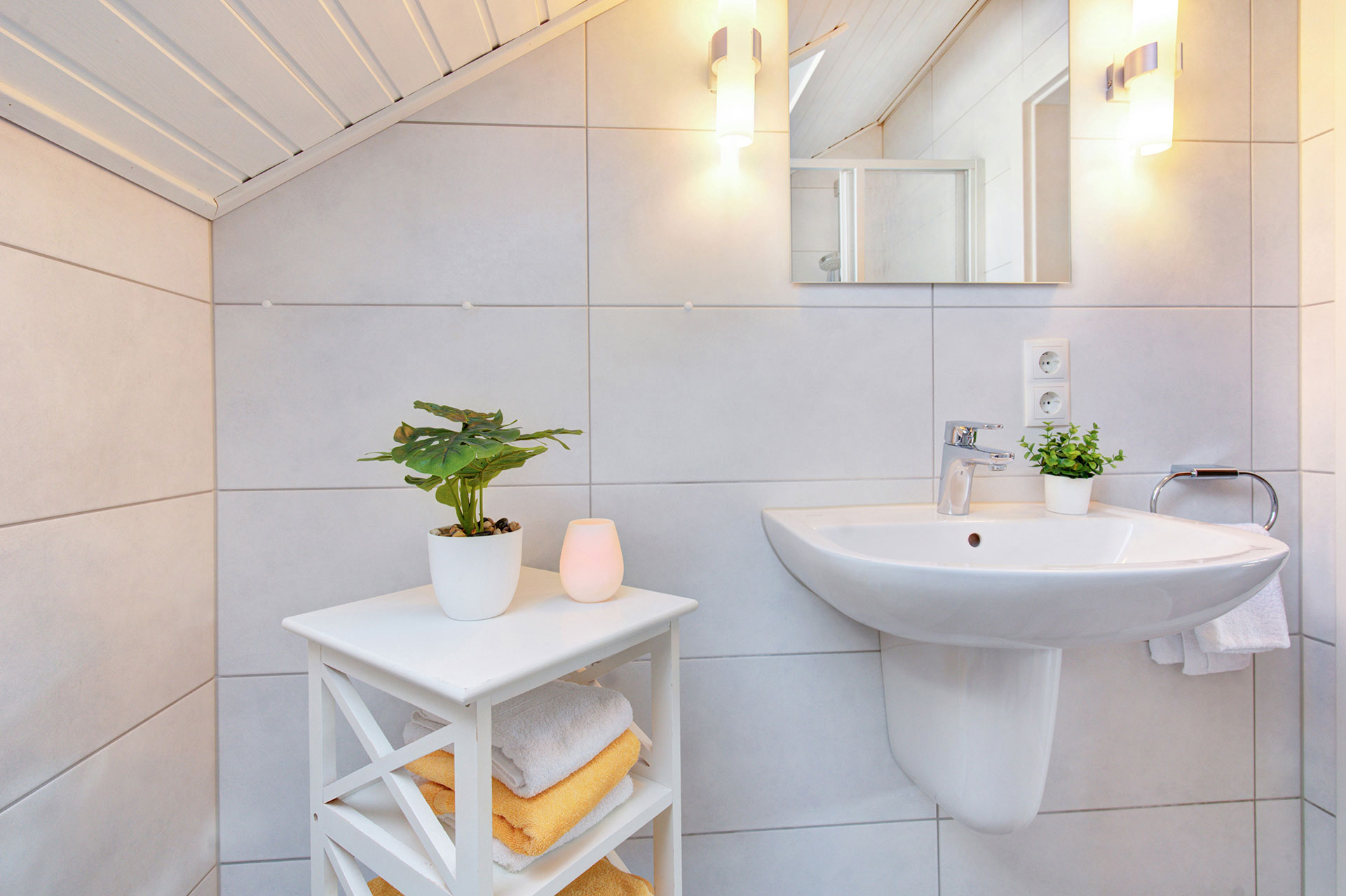 weises waschbecken und hochtisch mit akkuleuchte und grünpflanzen in ferienhaus
