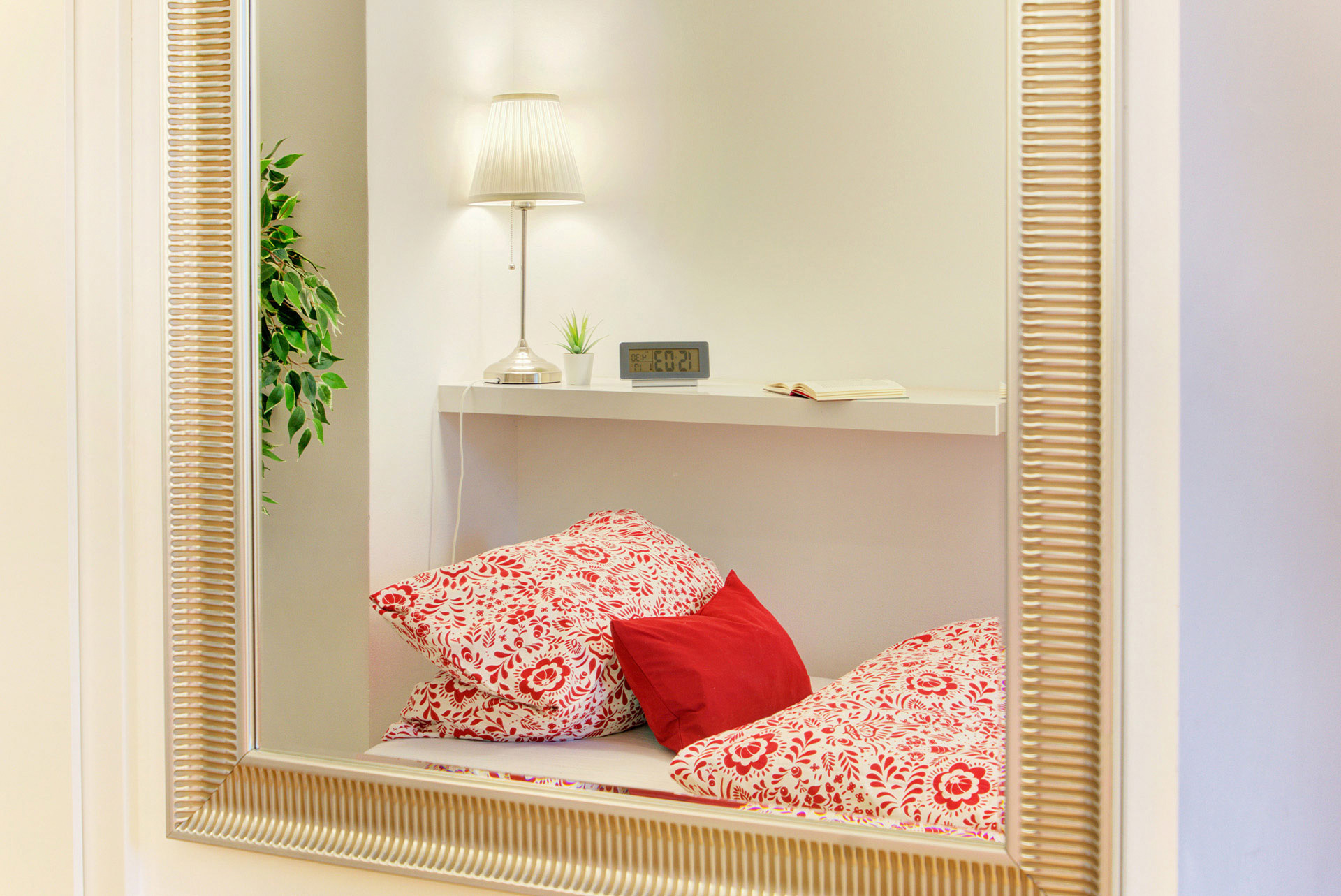 apartment fotografin blick in spiegel auf einzelbett mit rotem kissen