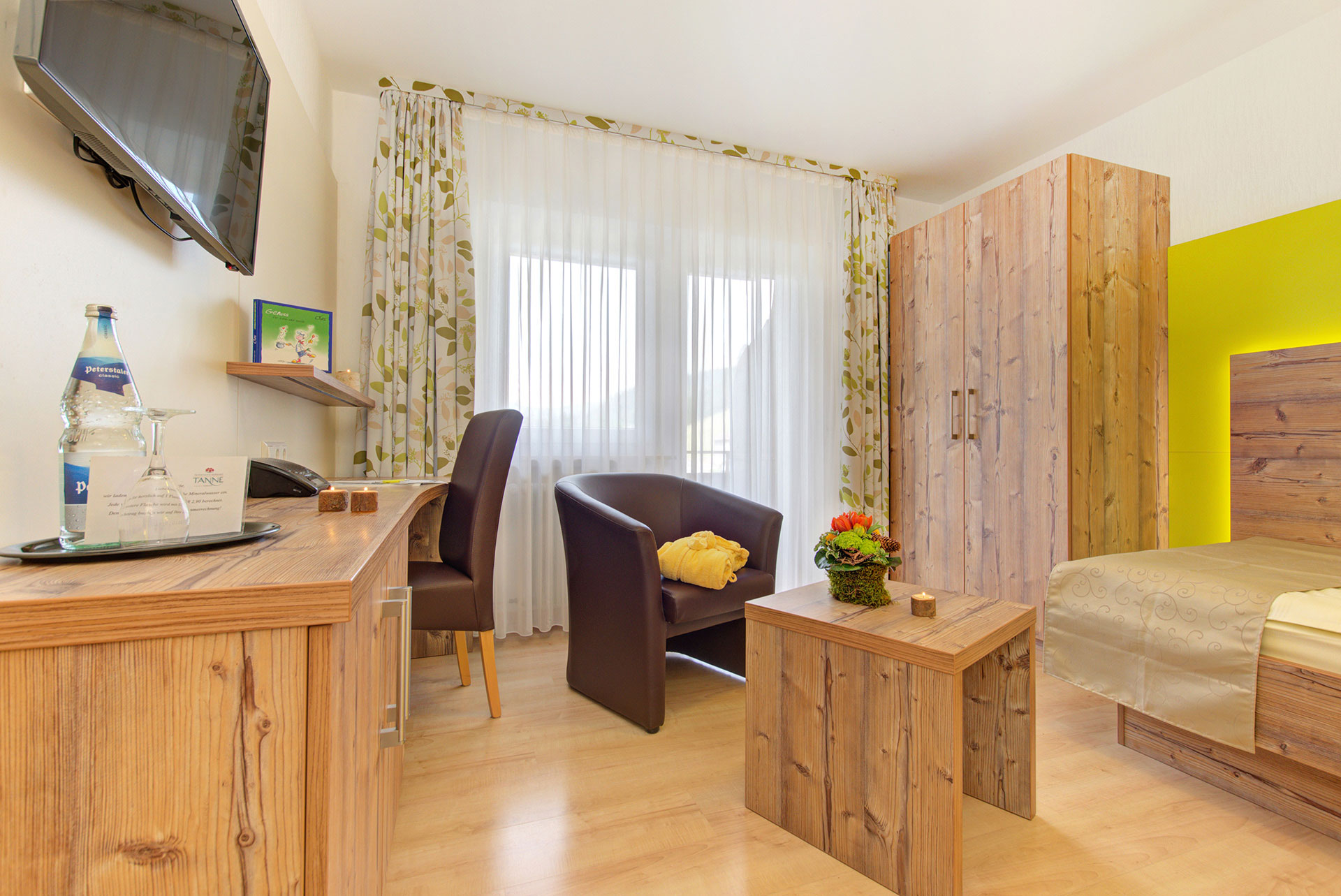 Einzelzimmer mit arbeitsbereich sowie sessel mit bademantel und tisch mit blumenbouquet in hotel