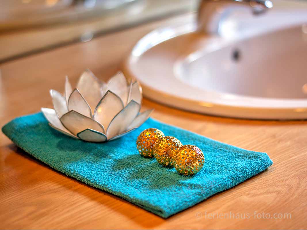 fotografin dekoriert lotusblüte und drei goldkugeln auf türkisem handtuch