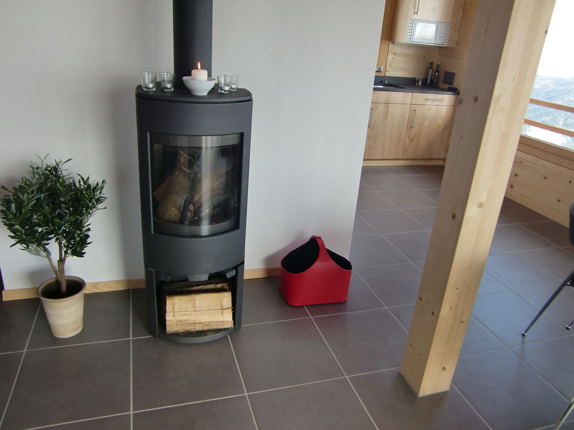 offenes Wohnzimmer in ferienhaus mit klassischem Schwedenofen sowie pflanze, holz und filztasche - vorher