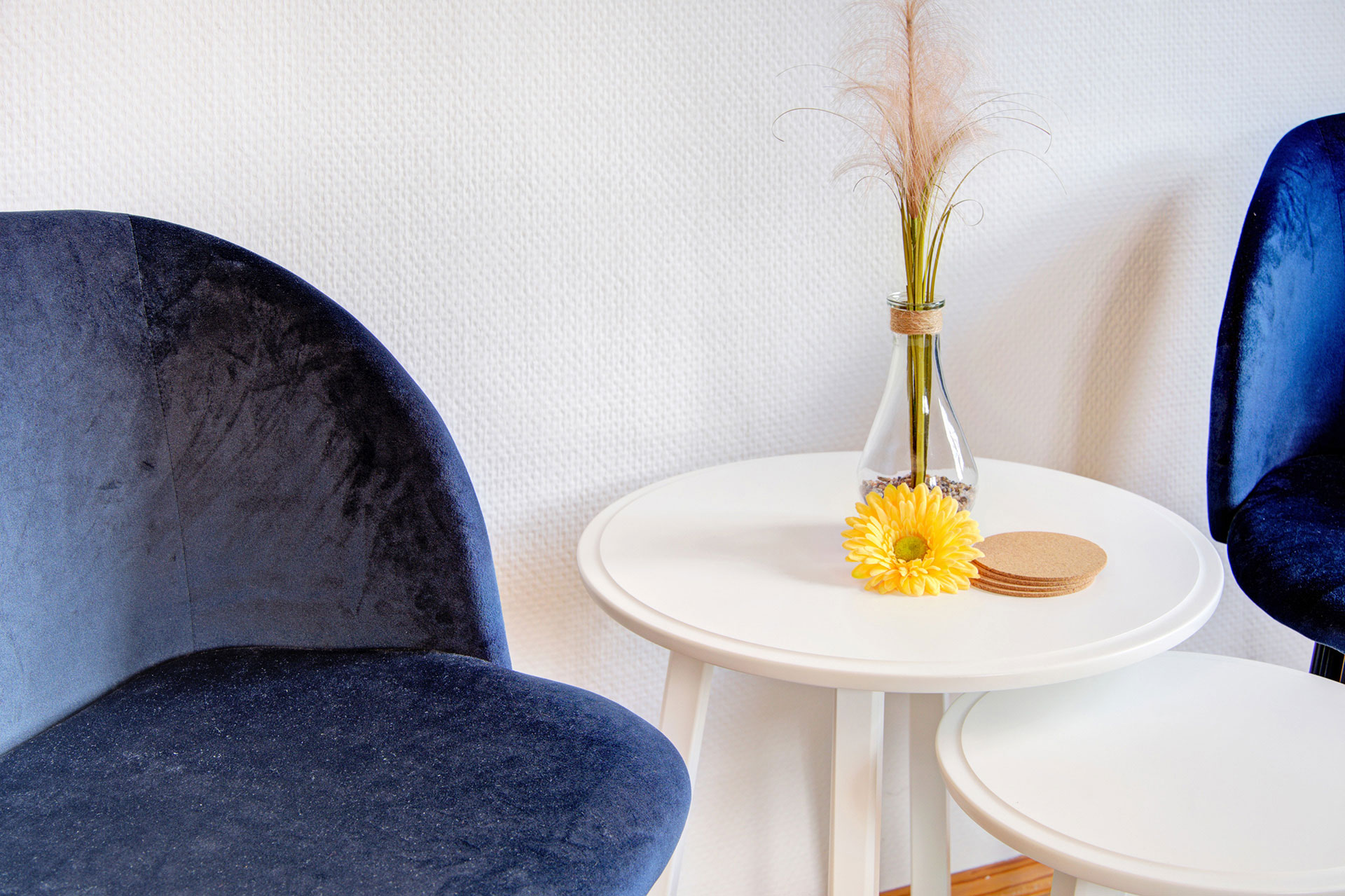 kleine sitzgruppe aus samtblauen stühlen tisch mit gelber gerbara und trockenblume in ferienhaus