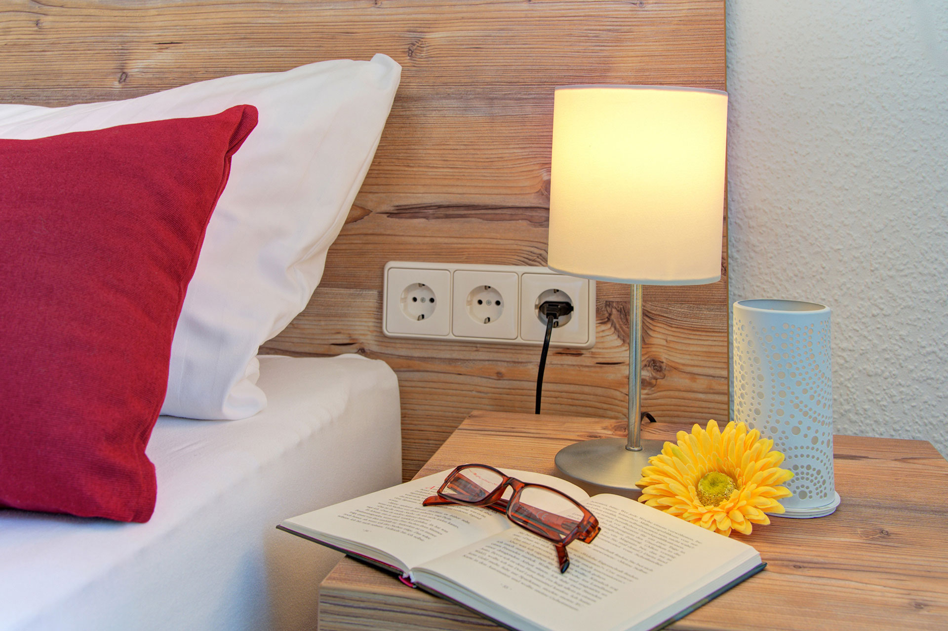 nachttisch mit buch brille gelbe gerbara und lampe in ferienhaus