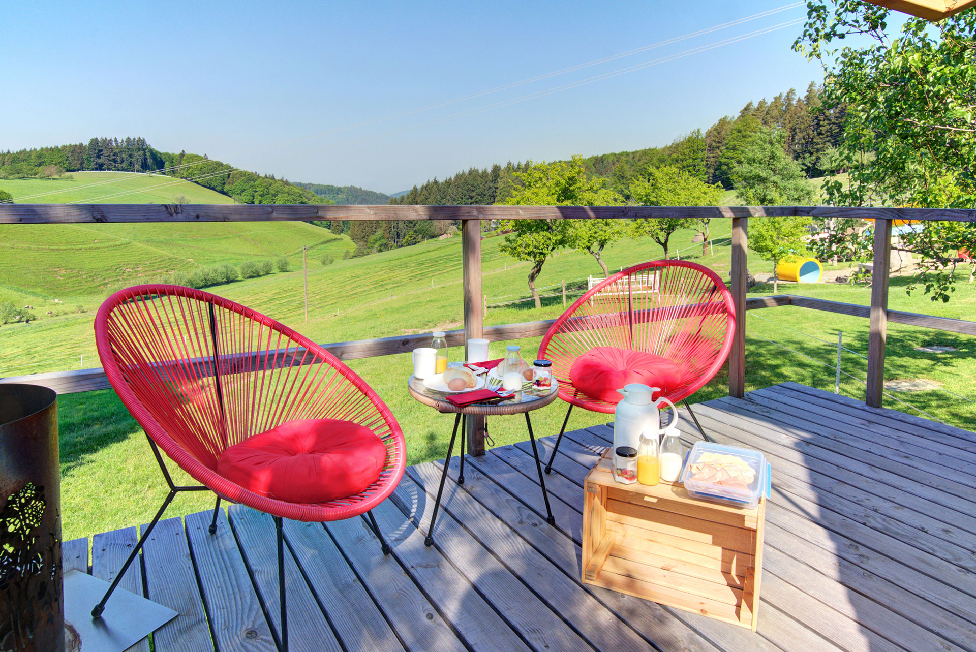 zelthaus mit terrasse mit zwei roten stühlen frühstückstisch und frühstücksbox mit blick auf landschaft und blauer himmel 
