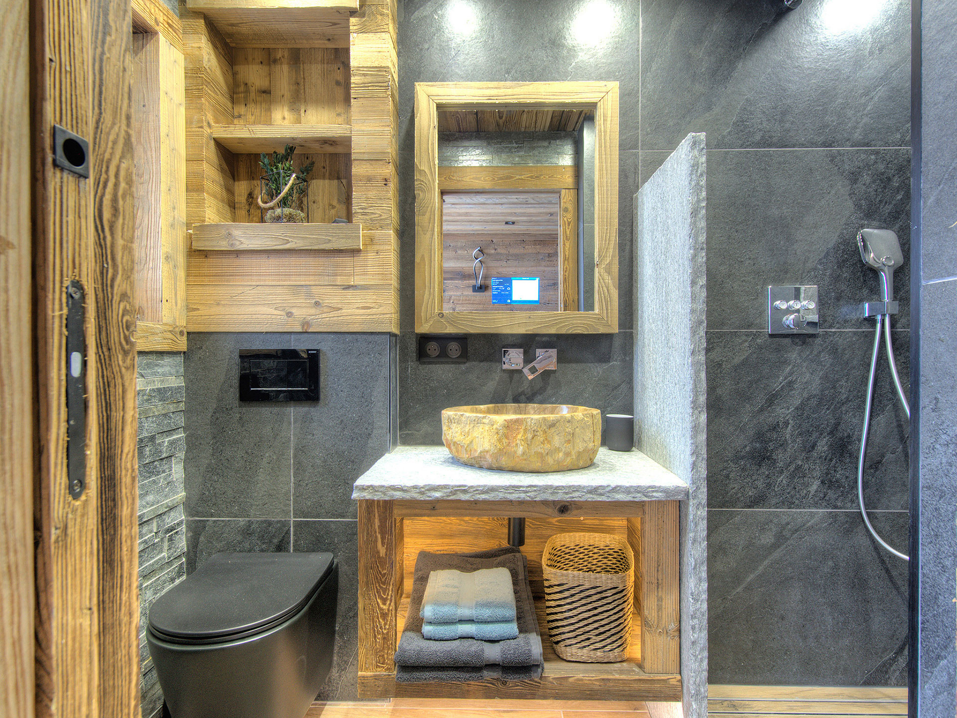 Badezimmer in Ferienimmobilie aus Holz und Naturstein mit Handtüchern und Fön