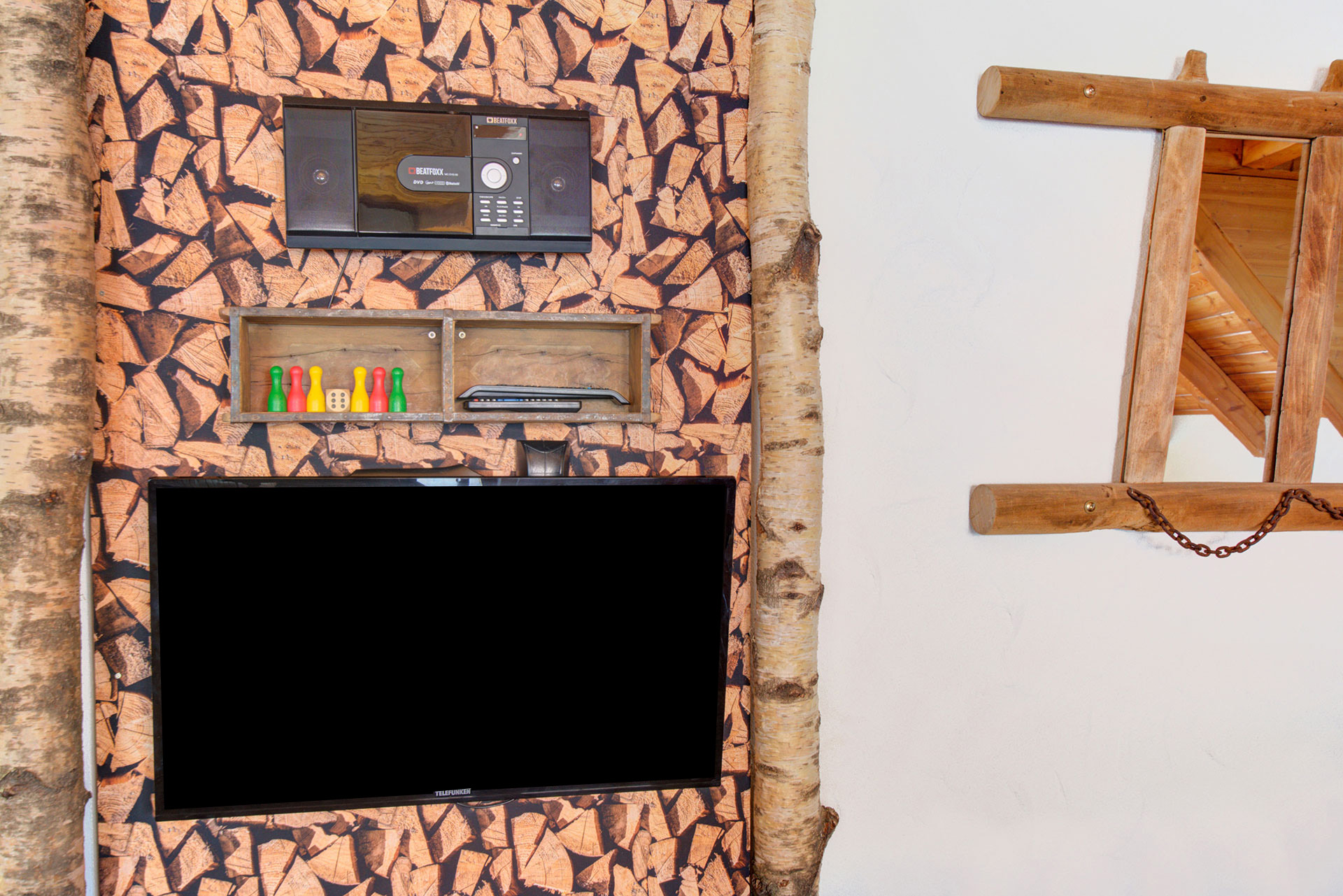Schwarzer Flachbildfernseher vor Holzwand mit Spielregal in einer Ferienwohnung, warme Holztöne - vorher