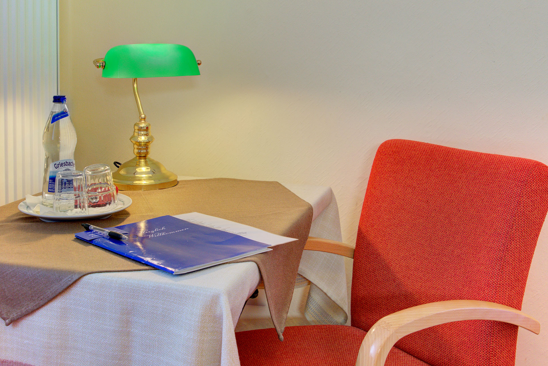 hotelfoto kleiner tisch und roter stuhl mit gruener lampe und getraenk sowie schreibzeug auf tisch