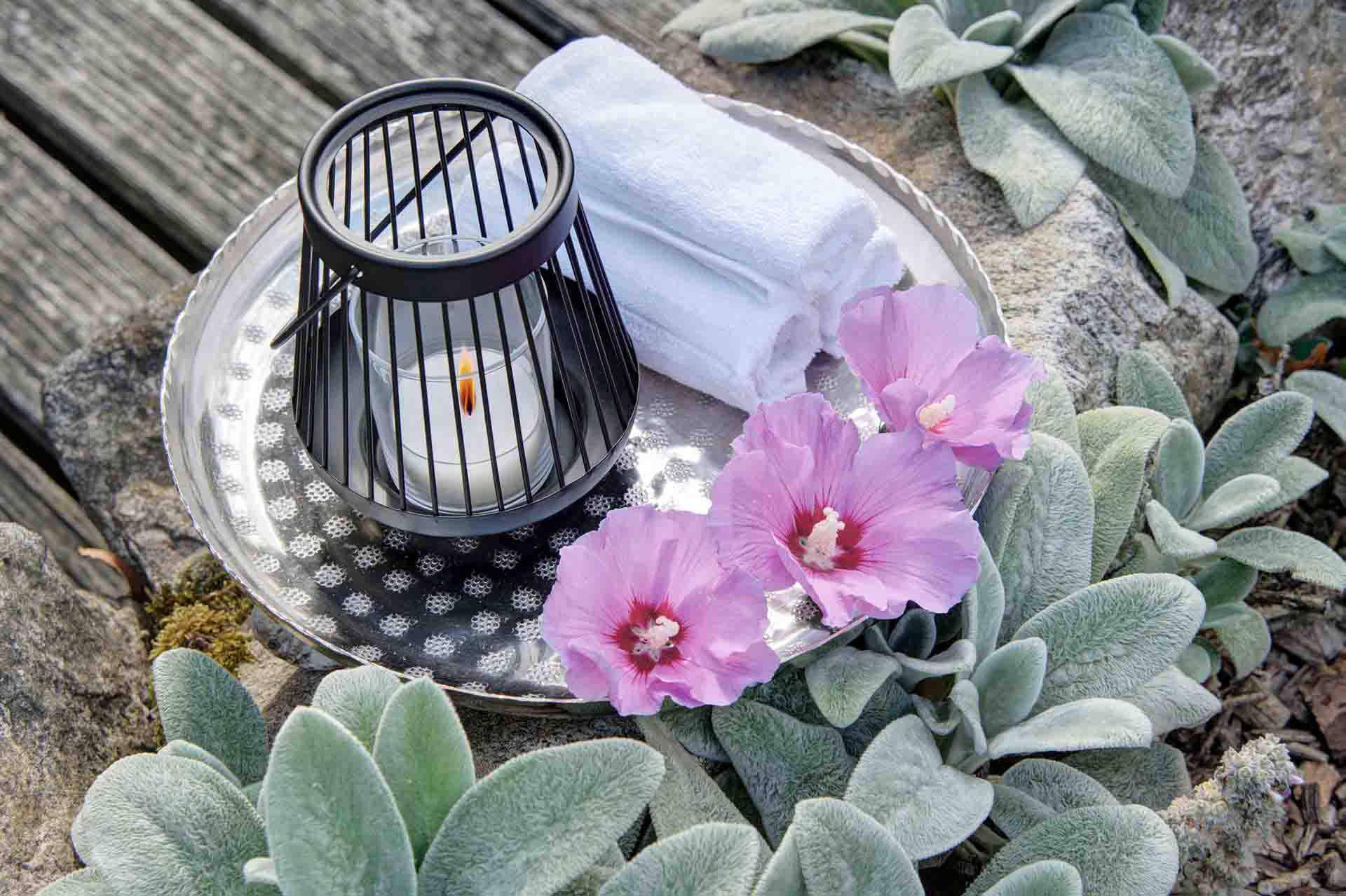 Silbertablerr mit schwarzem Teelicht, violetten hibiskusblüten und weisem handtuch im kräutergarten von ferienhof