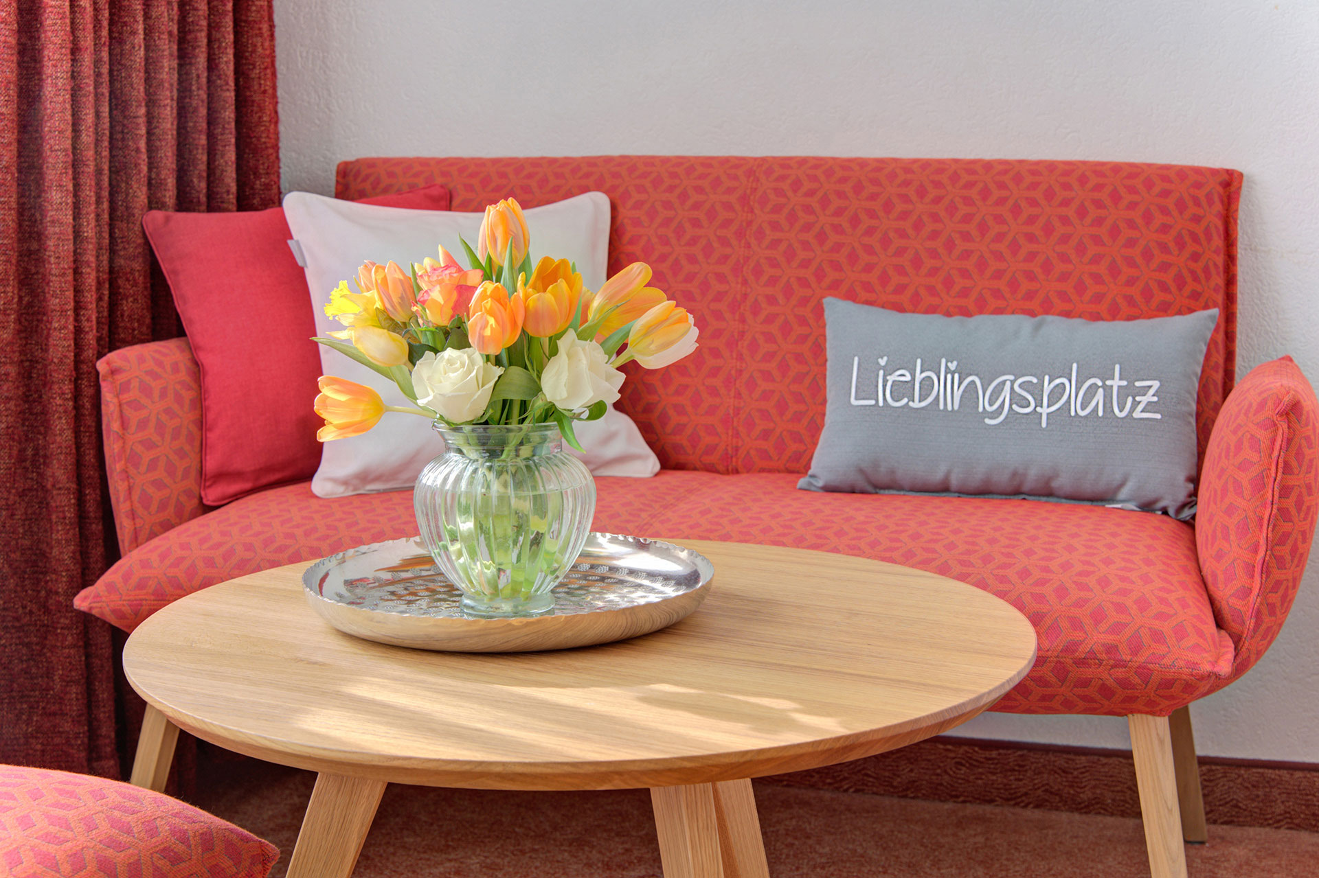 tisch mit blumenstrauss vor rotem sofa mit lieblingsplatzkissen in hotel