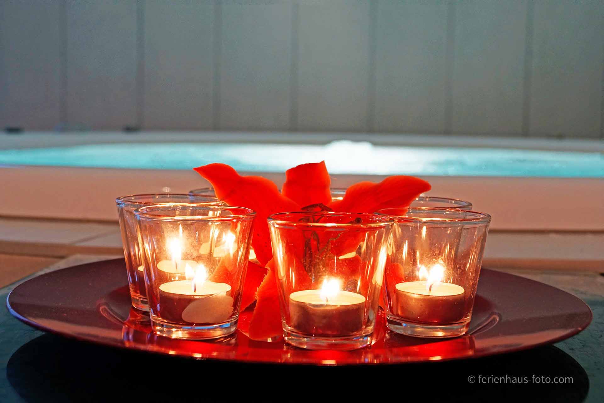 hotelfotograf rotes tablett mit teelichtern roter lilienblüte vor türkisem whirlpool