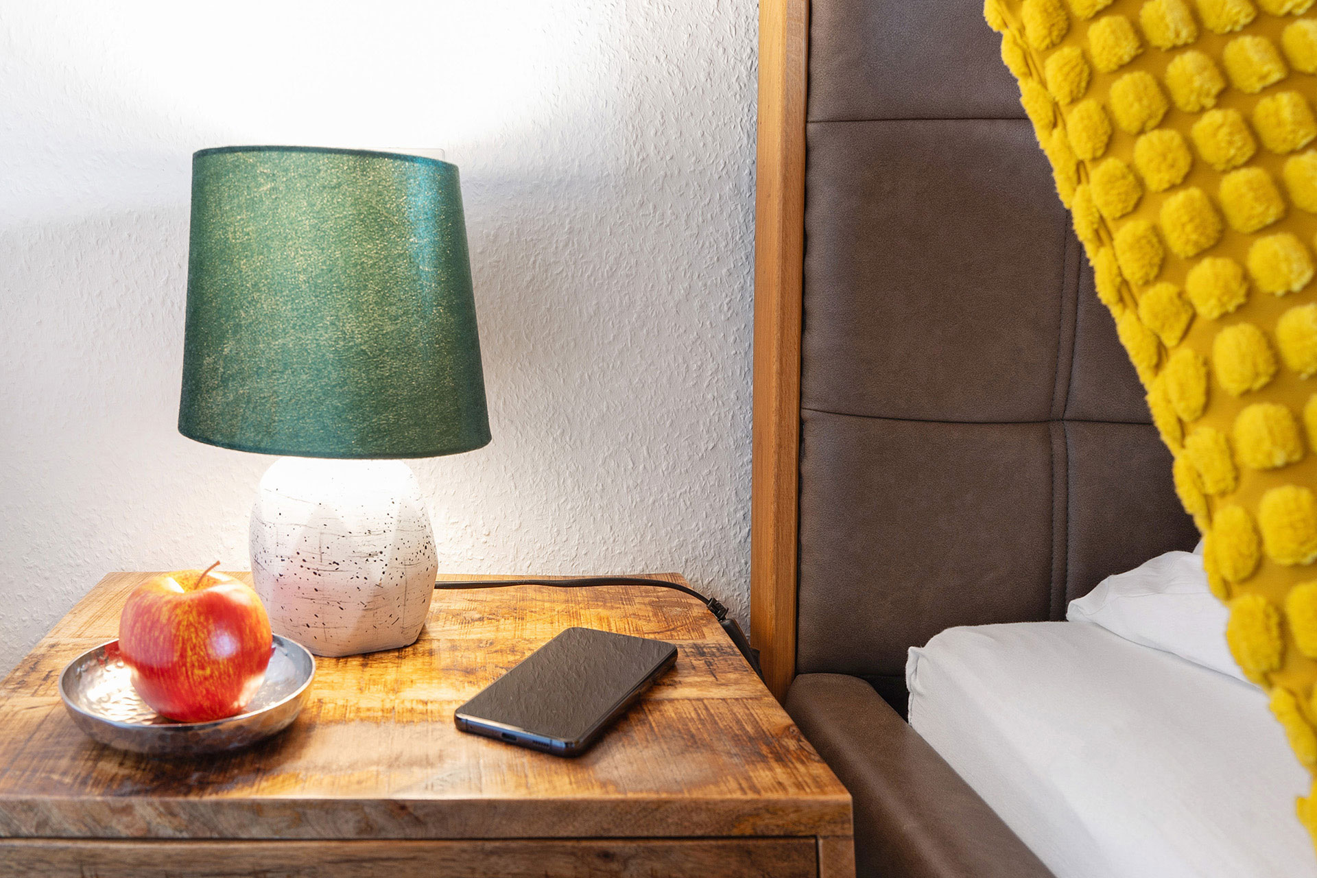 nachttisch mit grüner lampe apfel und smartphone in ferienwohnung