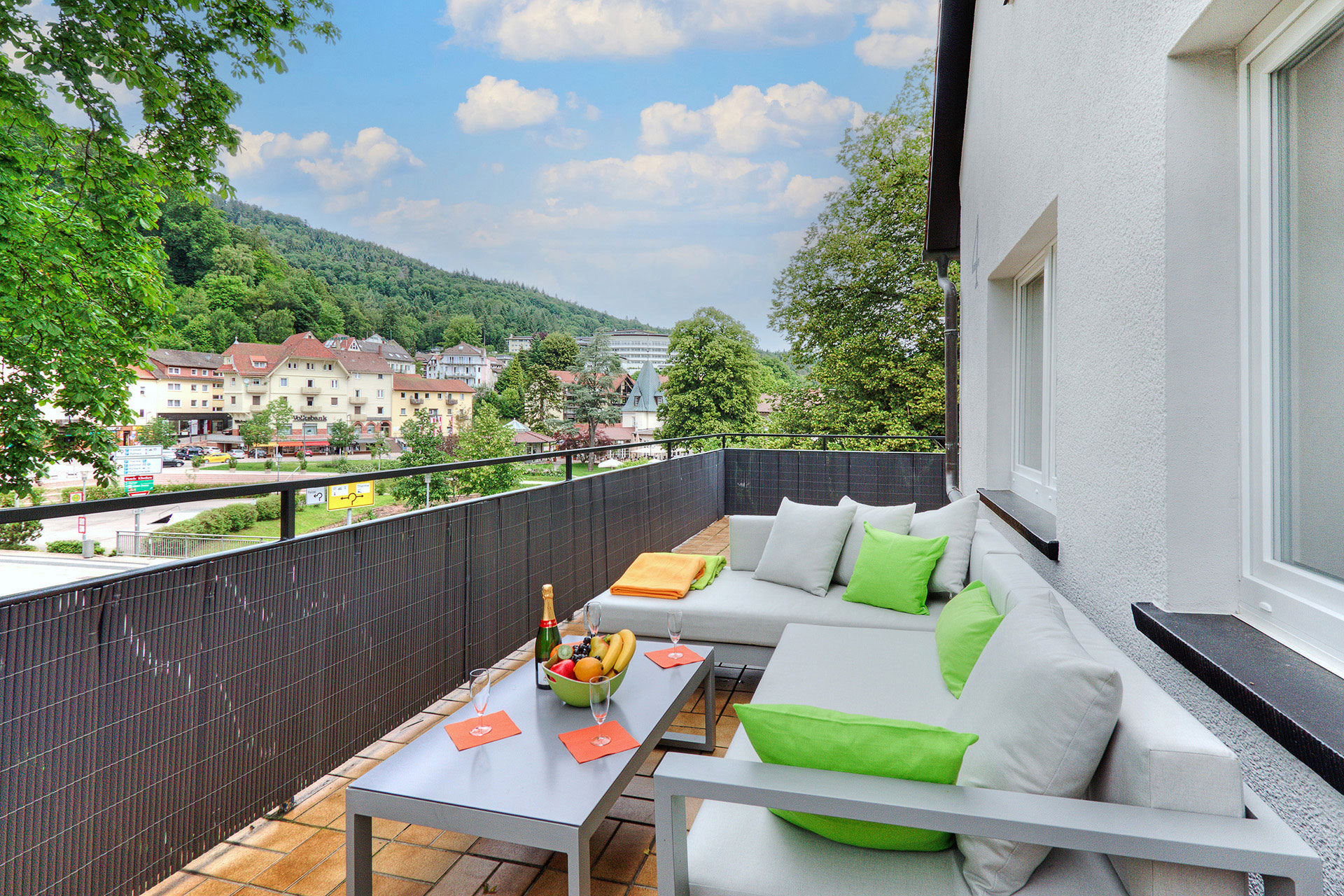 sofagarnitur auf balkon mit grünen Kissen und Sekt sowie Obstkorb und blick auf bad herrenalb in ferienwohnung