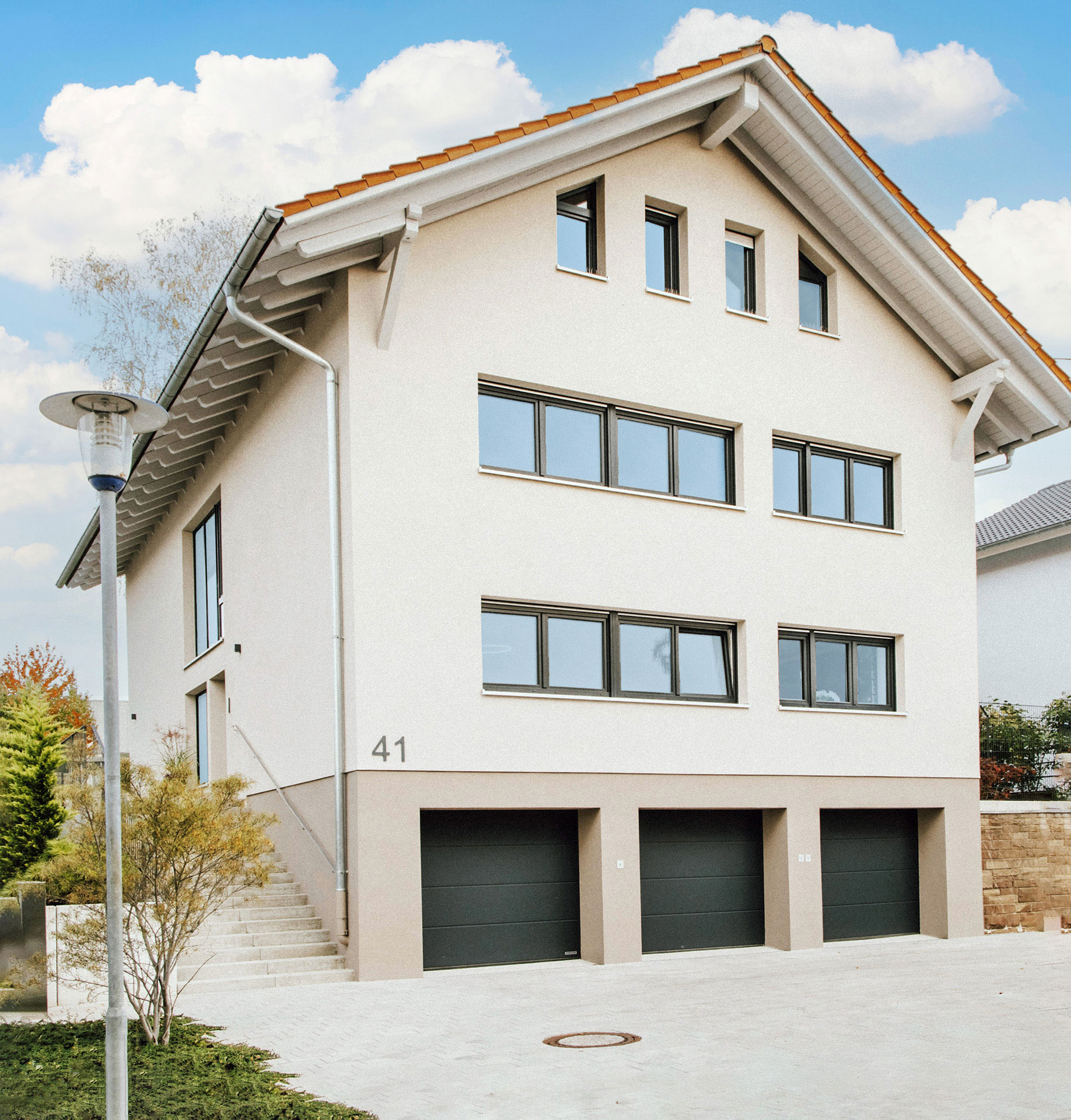 Modernes Wohnhaus, starker Kontrast zu blauem Himmel, wenige Wolken, sonnige Atmosphäre - nachher