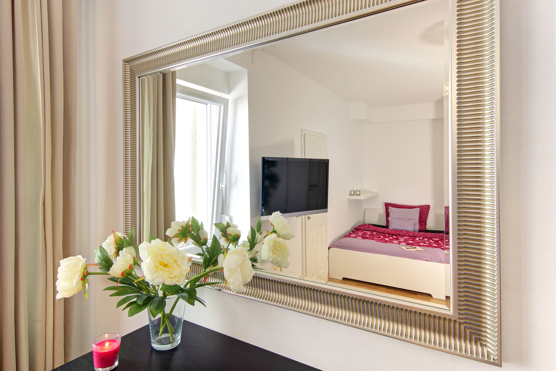 fotografin dekoriert grosse pfingstrosenstrauss vor spiegel mit blick auf einzelbett und tvmonitor