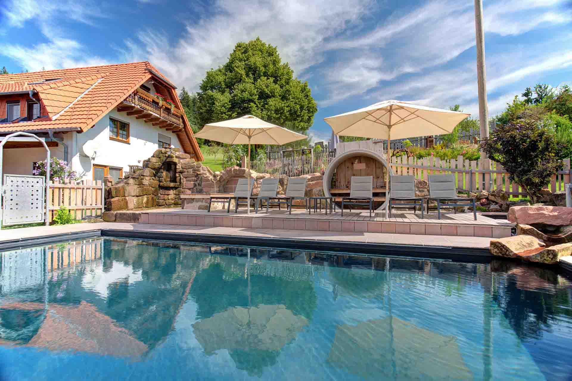pool am ferienhaus mit Schirmen und Liegen im Sommer bei blauem himmel