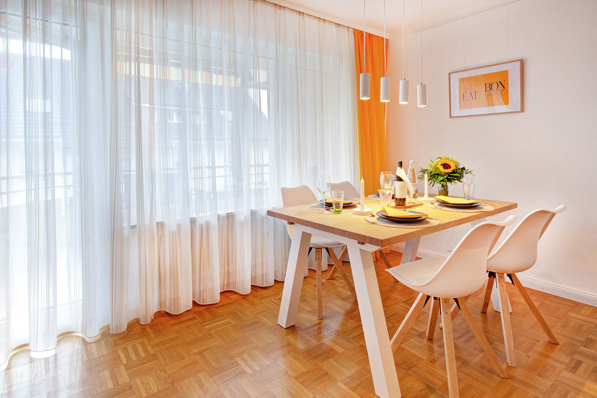 Essbereich der ferienwohnung mit blumenstrauss und blick auf gardinenfenster