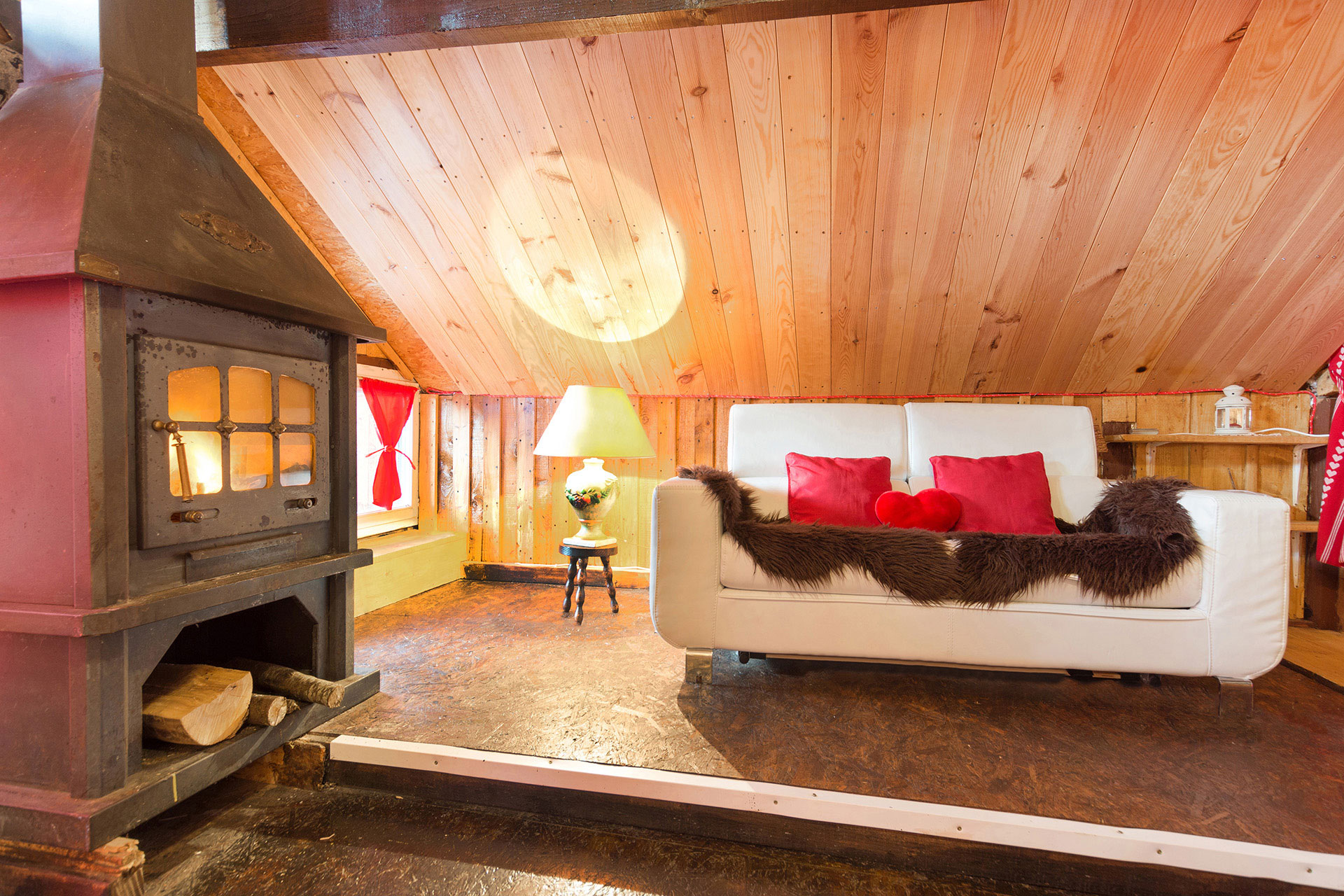 ferienhaus foto wohnzimmer mit offenem kamin und cremfarbenen sofa geschmueckt mit roten kissen und schwarzem fell