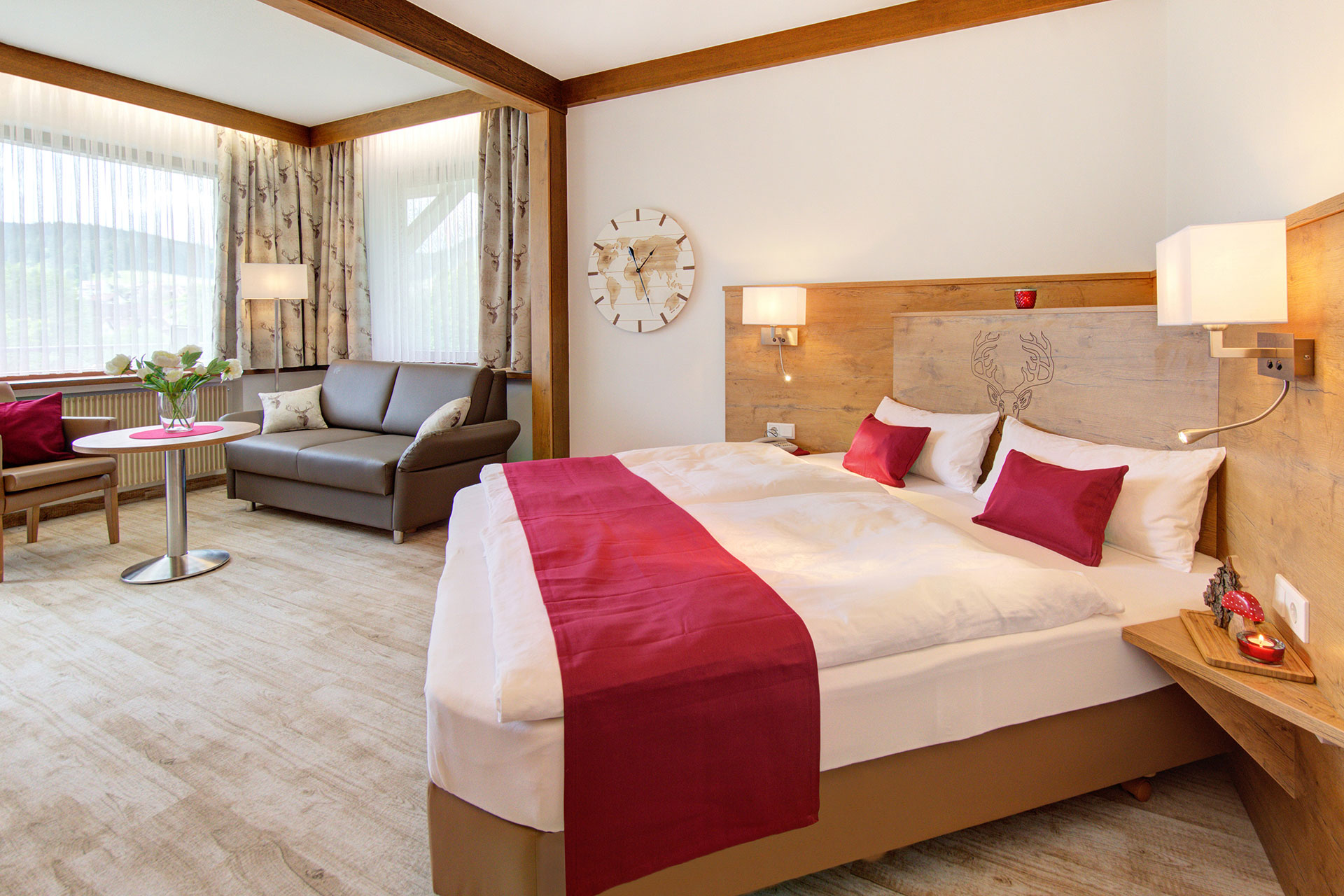 foto ferienwohnung doppelzimmer mit rotem bettlaeufer und kleinen roten kissen mit blick auf sofa und fenster
