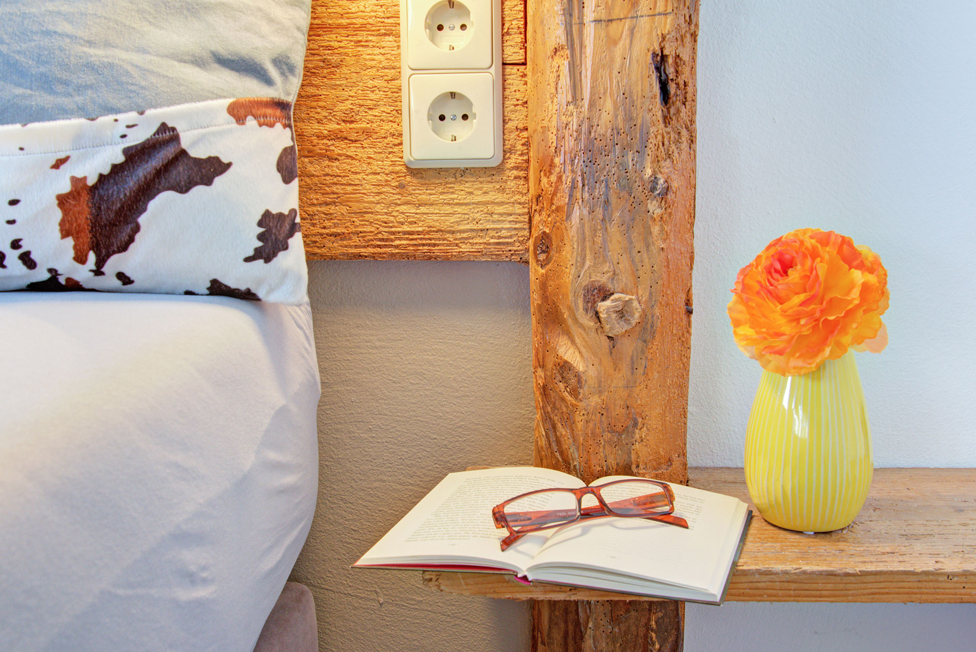 nachttisch mit buch brille und orangener gerbara in Ferienwohnung
