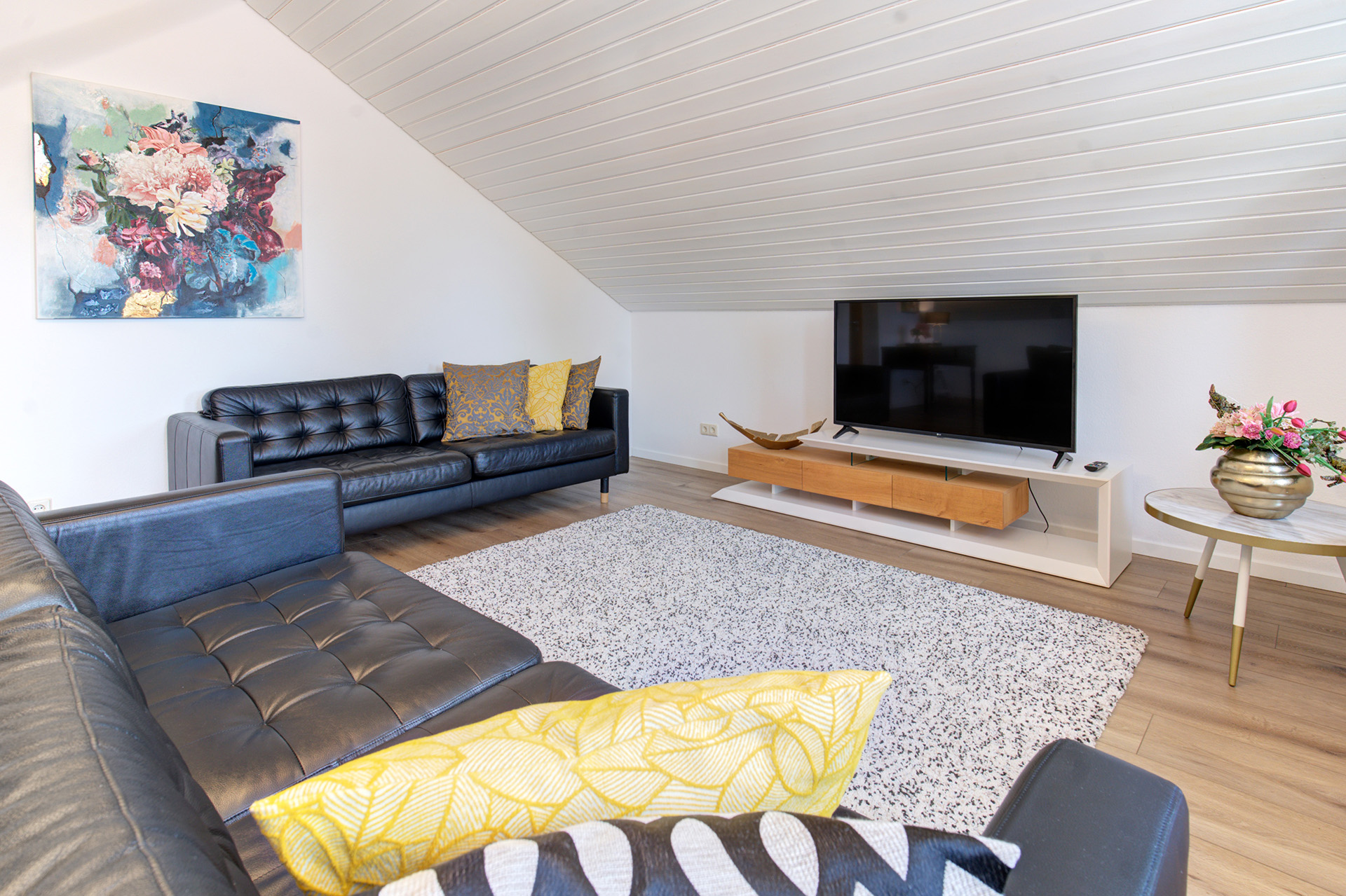 Helles Wohnzimmer der Ferienwohnung mit Sofas, buntem Blumenbild und Flachbild-TV