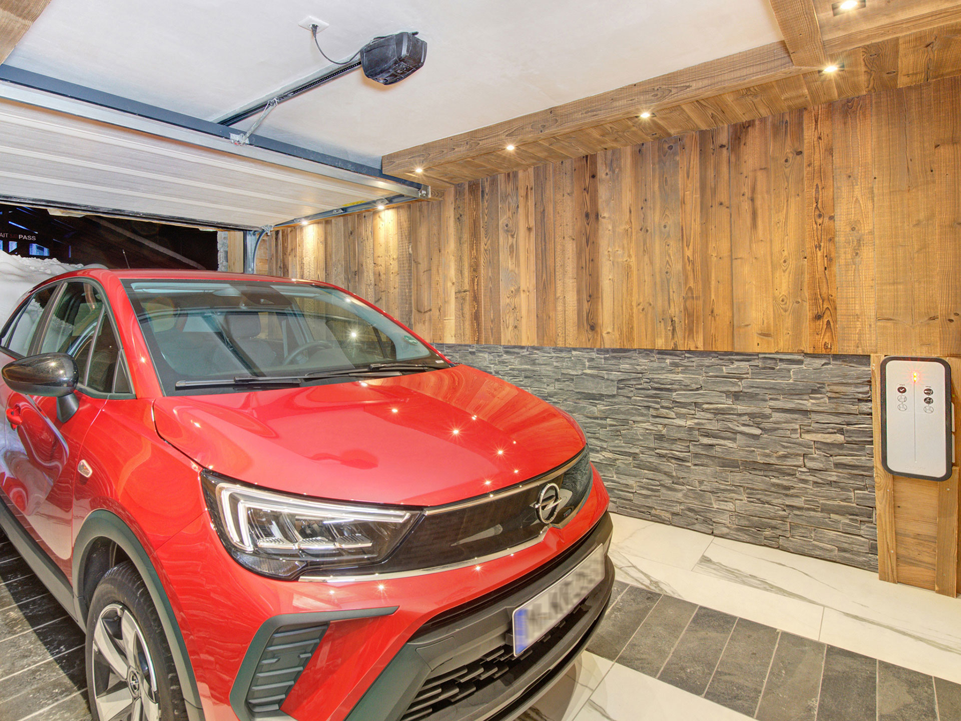 Garage aus Holz und Stein mit E-Zapfsäule und rotem Fahrzeug