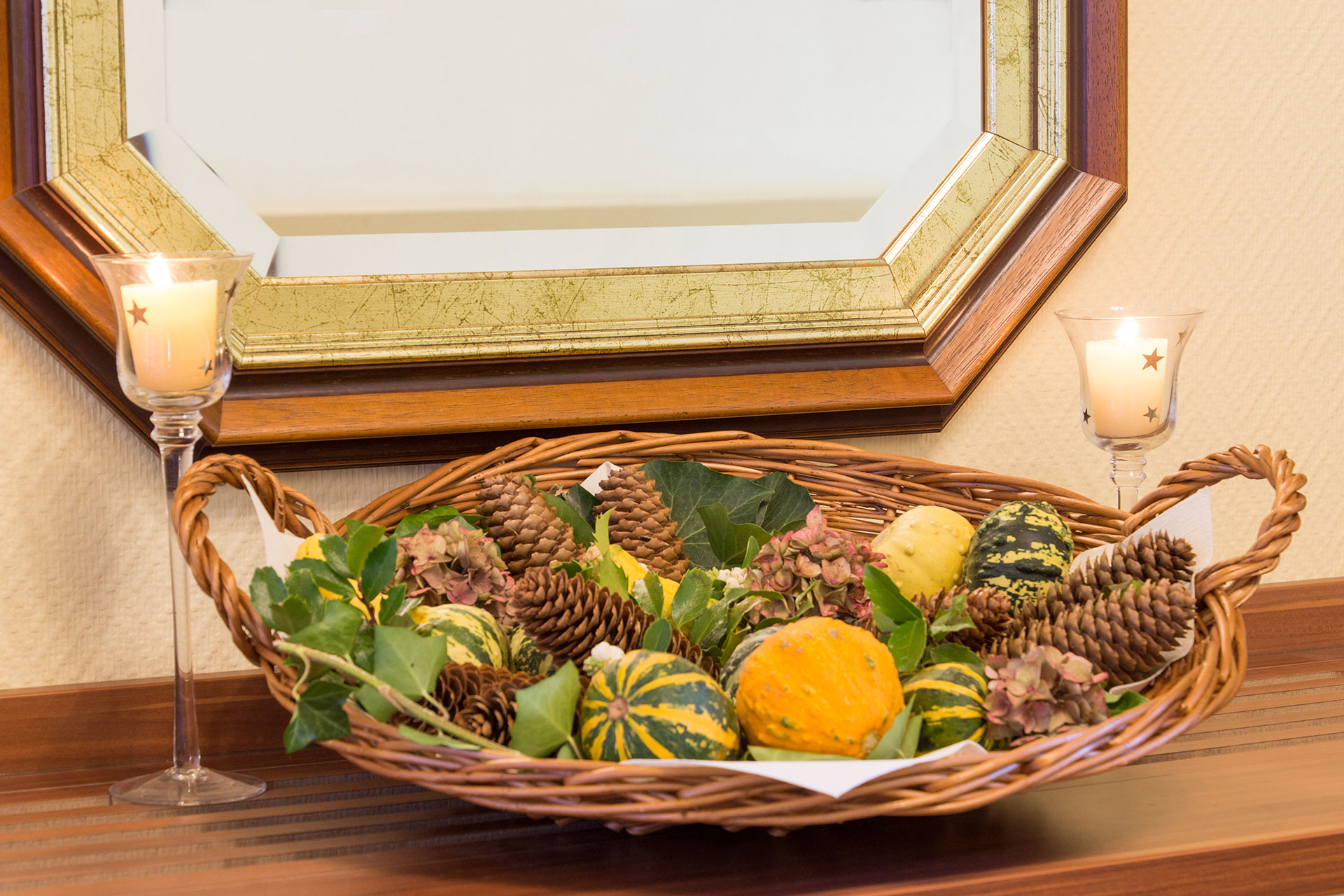 hotelfoto korbschale mit kleinen kuerbissen und tannenzapfen daneben teelichtern 